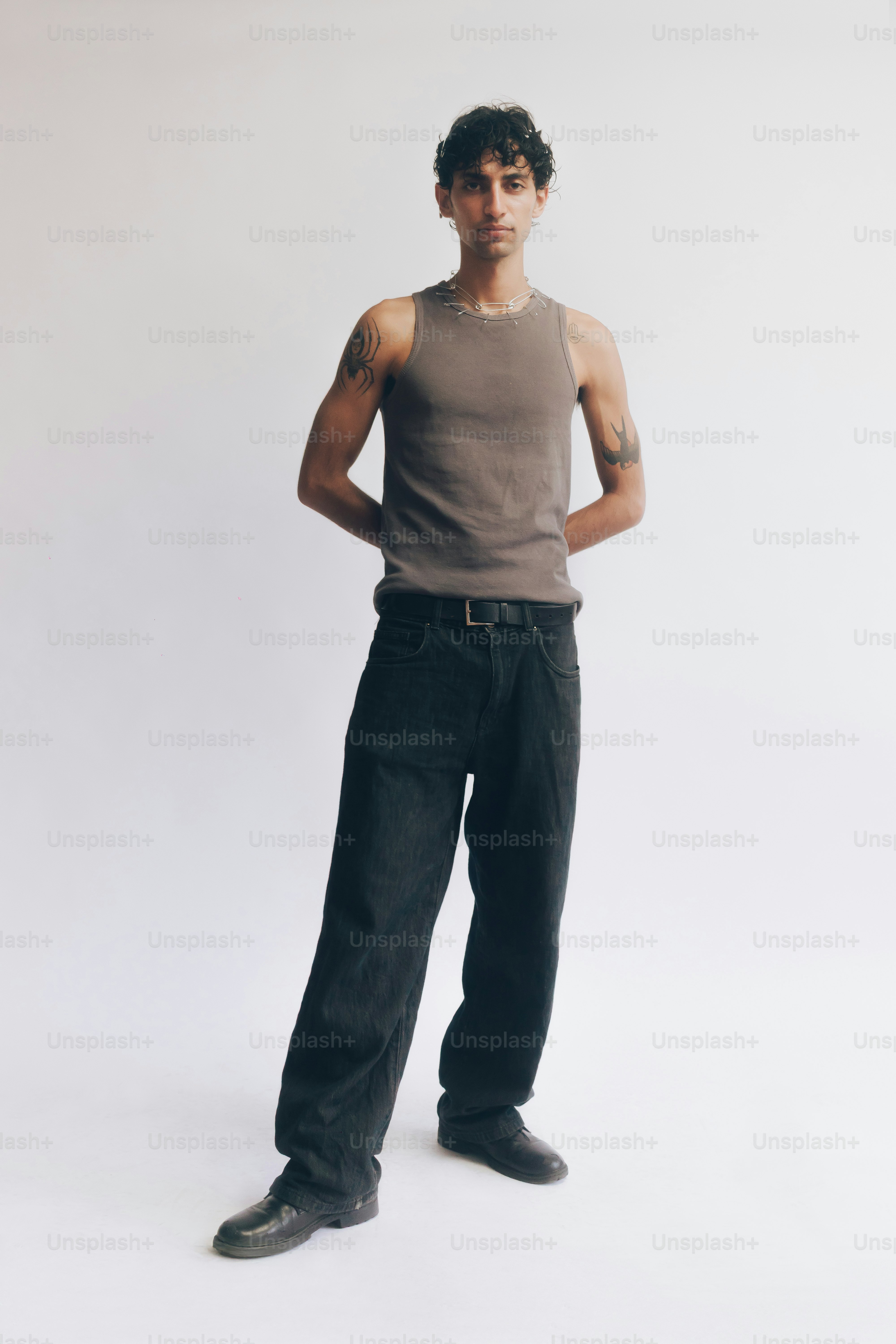 Eine Person mit Tattoos, die ein graues Tanktop und schwarze Jeans trägt