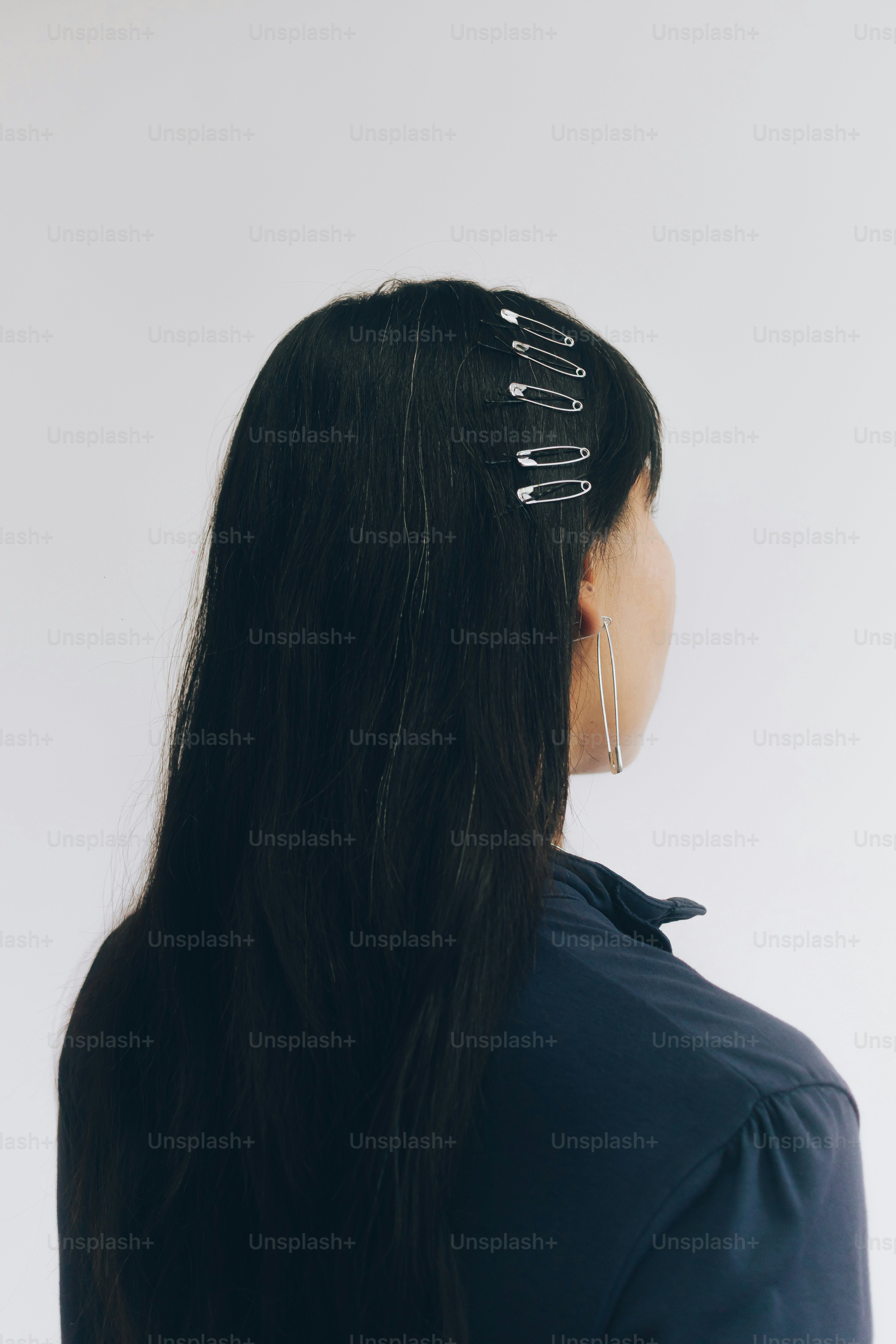 Eine Person mit langem dunklem Haar, das mit silbernen Sicherheitsnadeln als Clips gestylt ist