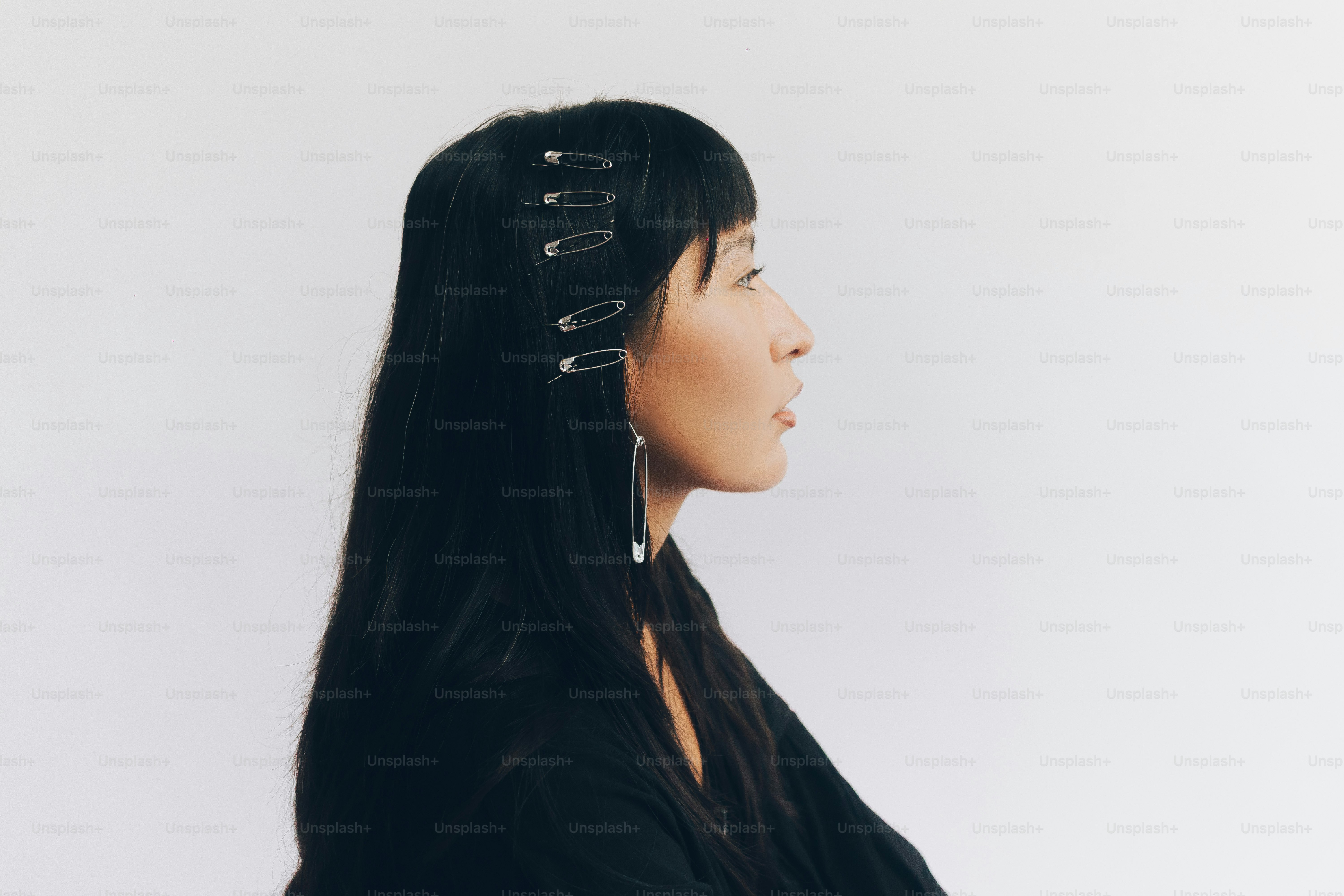 A woman with long dark hair styled with silver safety pins in profile