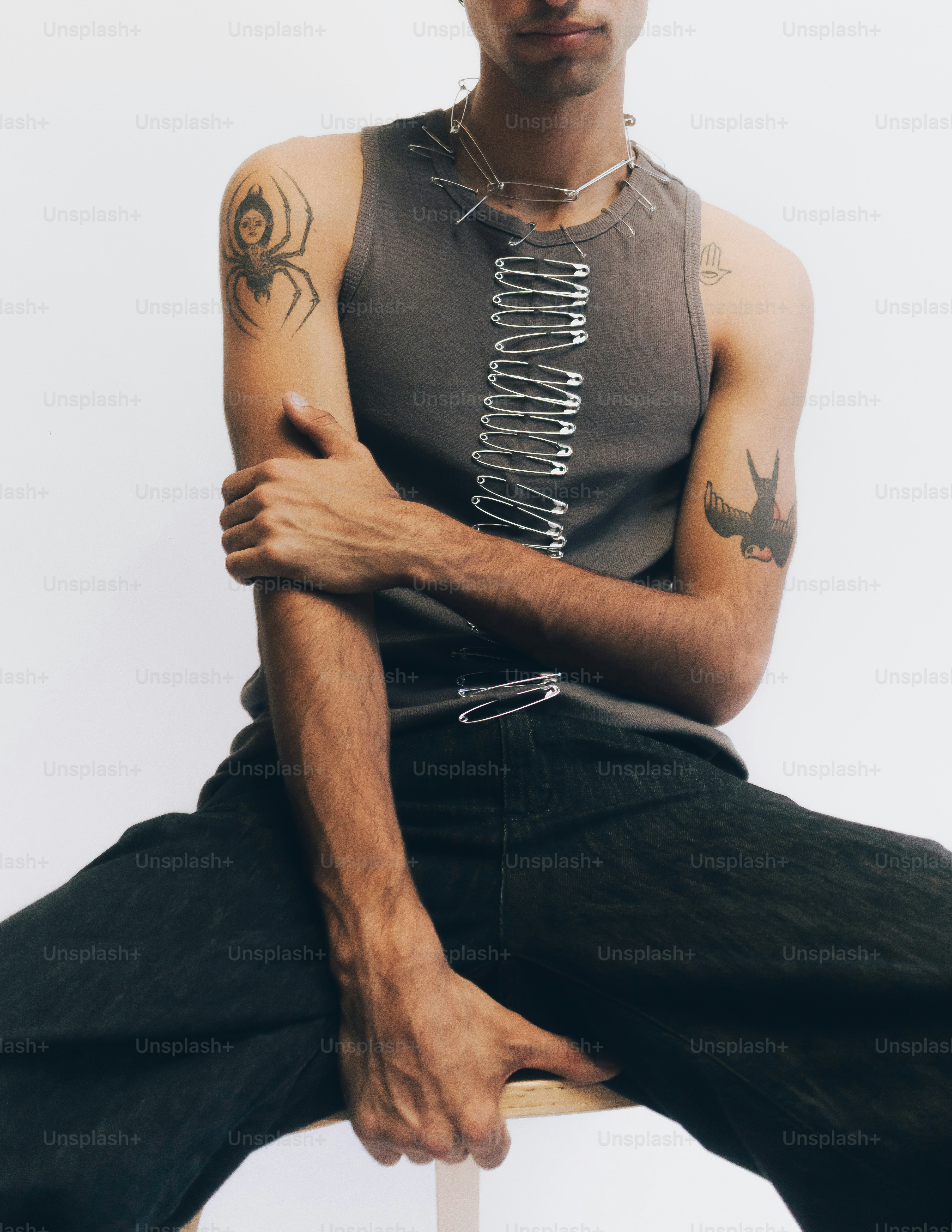Eine Person in einem grauen Tanktop, verziert mit Sicherheitsnadeln und Tattoos
