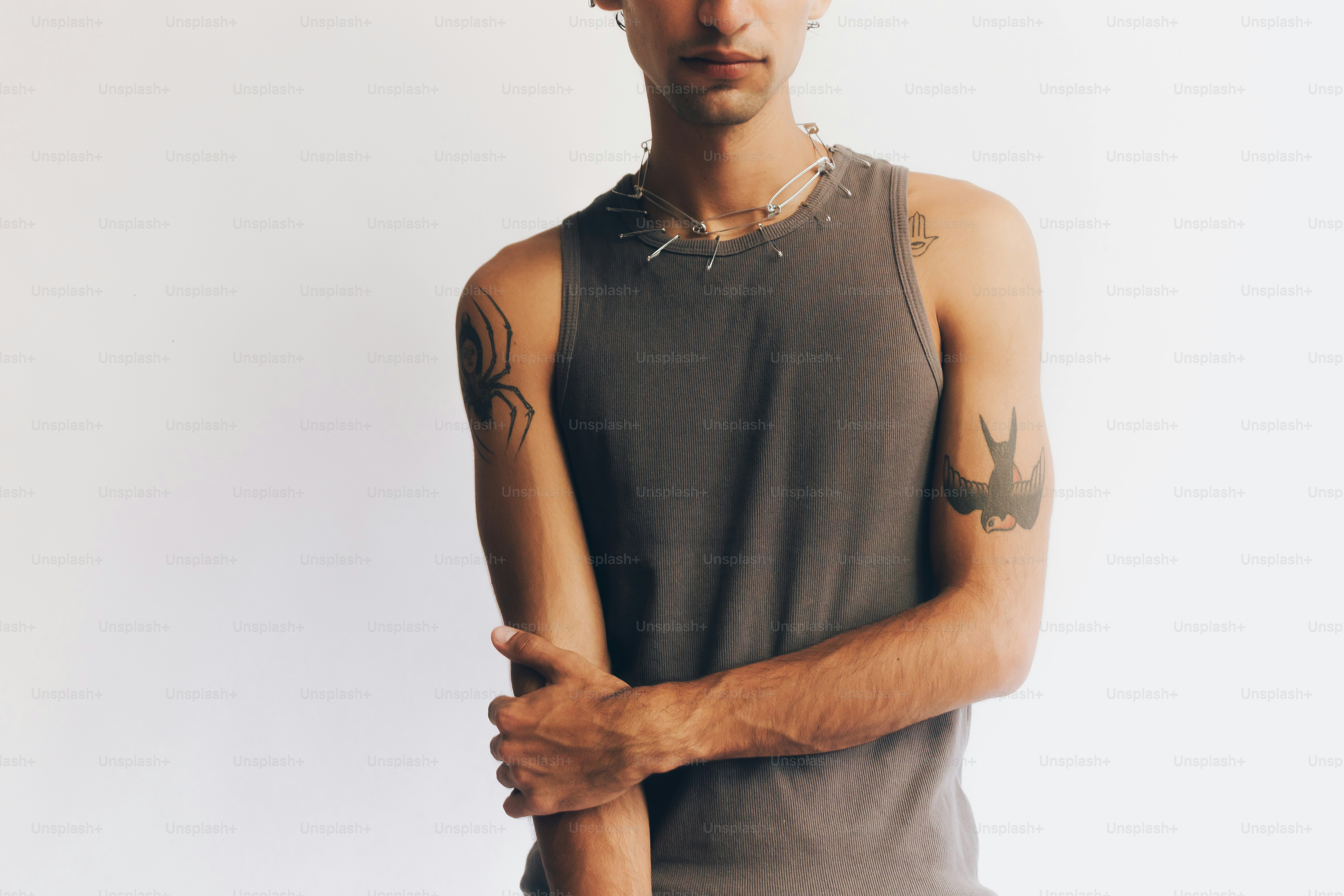Eine Person in einem grau gerippten Tanktop mit Spinnen- und Vogel-Tattoos