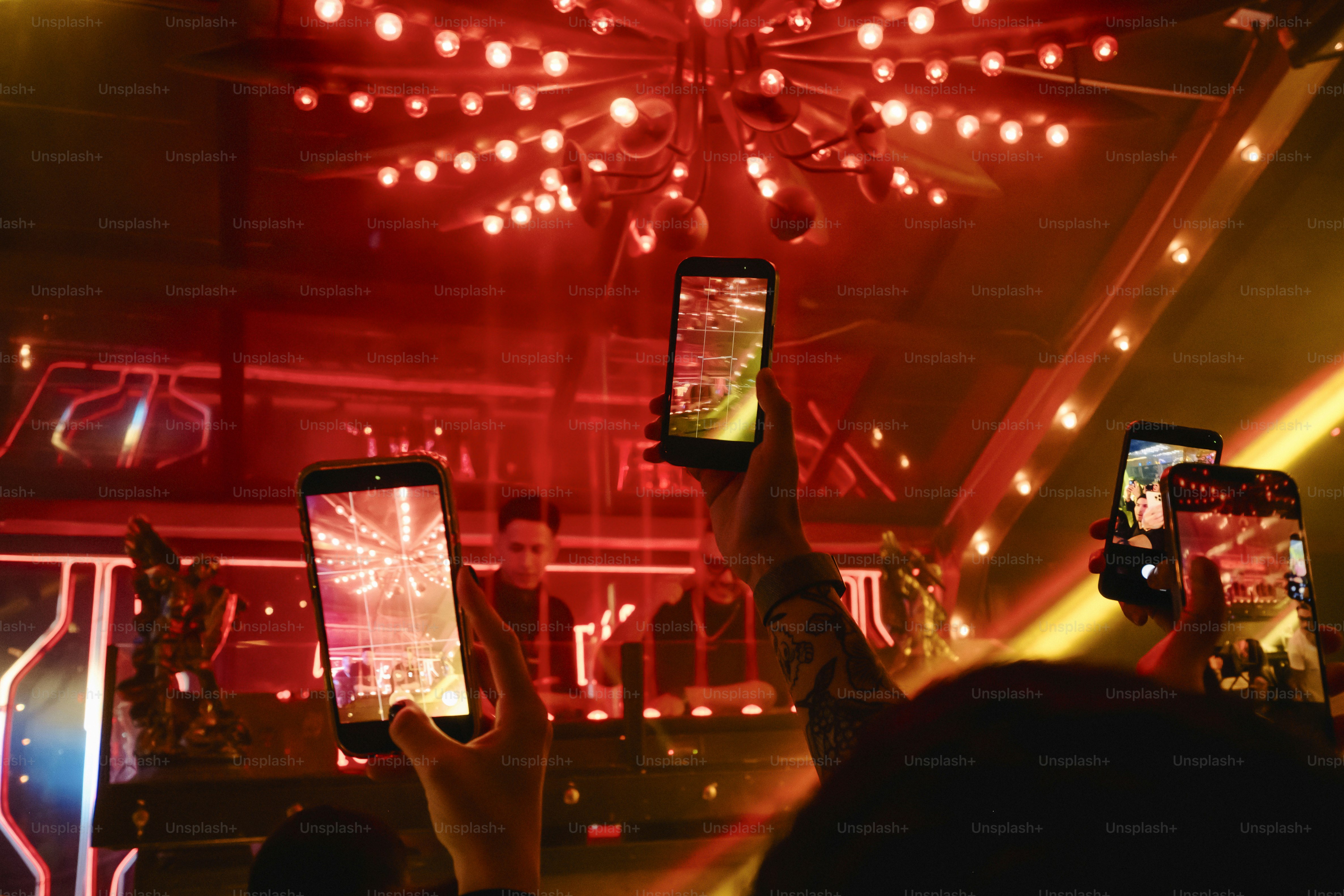 People holding up smartphones to record a DJ in a red-lit nightclub