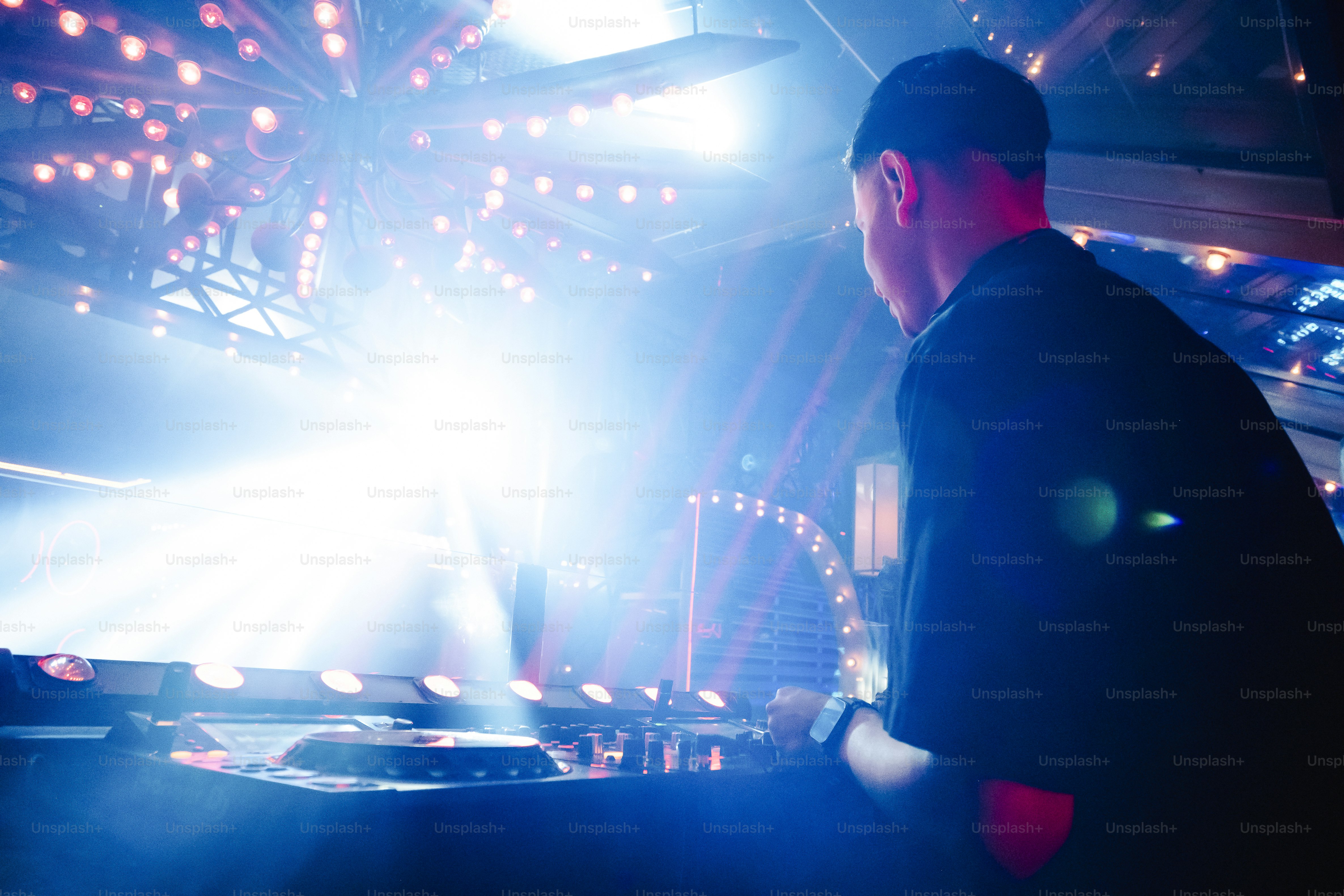 A person operating a DJ mixer in a nightclub with bright stage lights