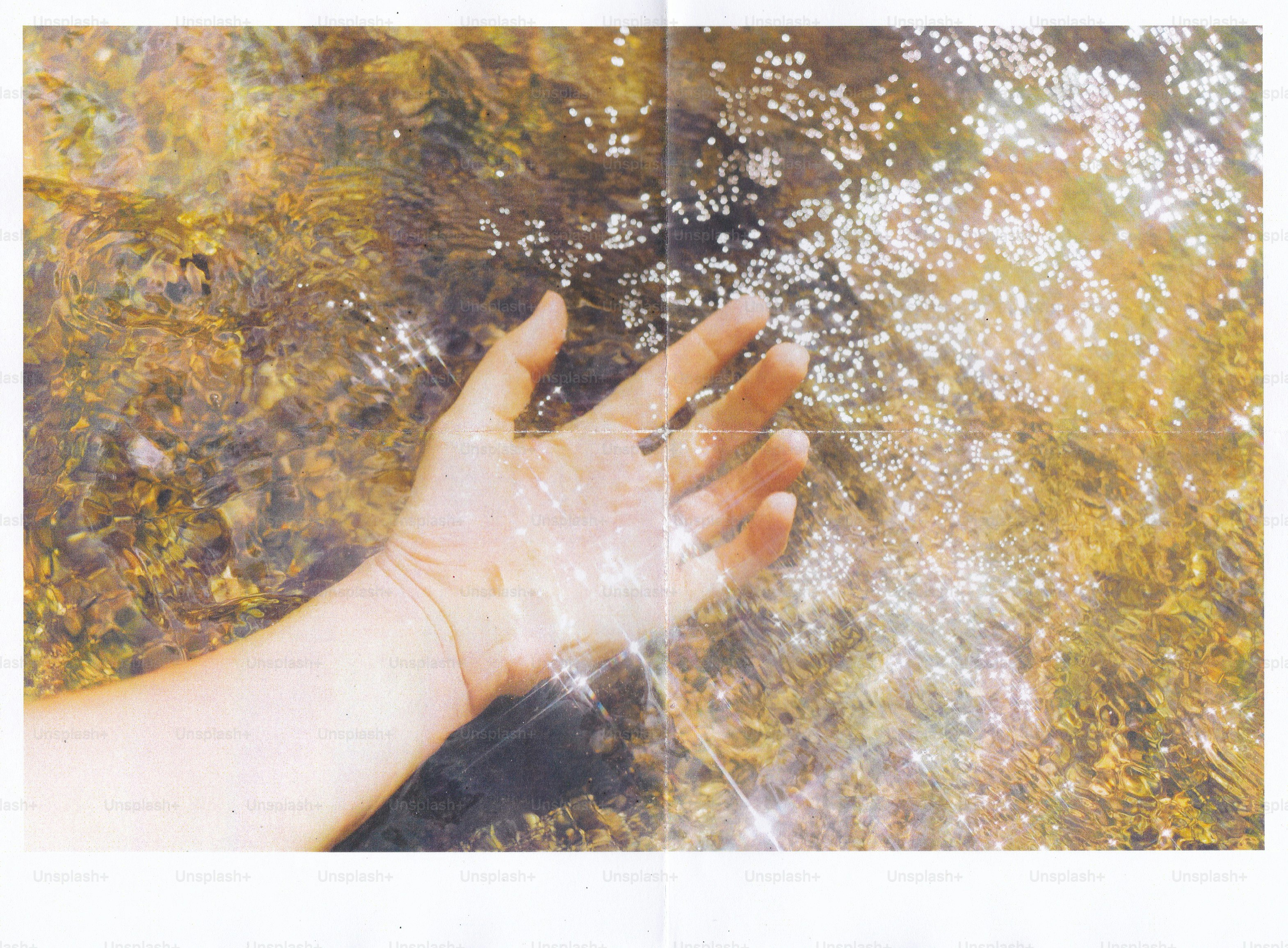 A person's hand submerged in shallow sunlit water with sparkling light reflections