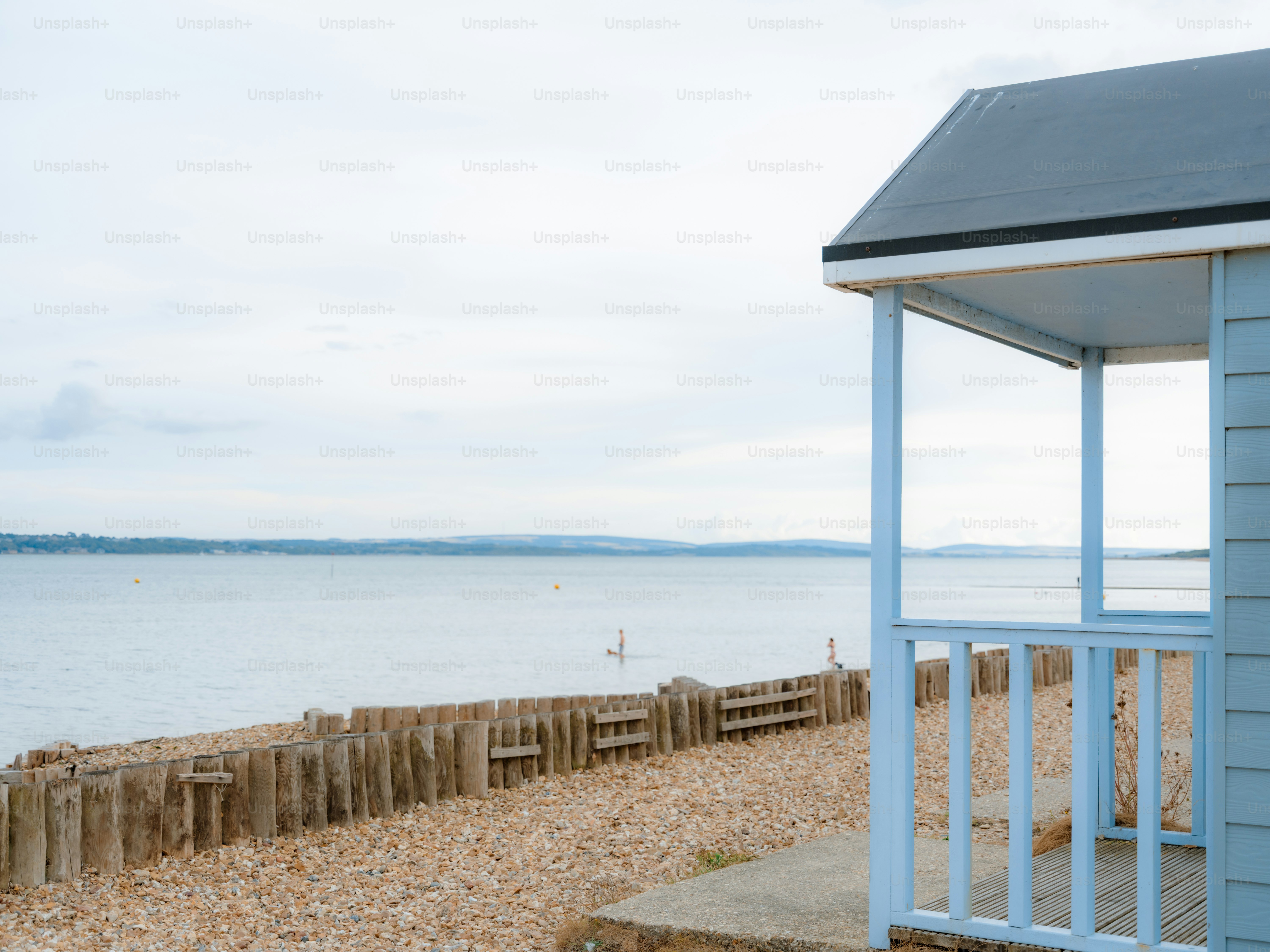 A light blue beach hut on a pebble shore overlooking a calm bay