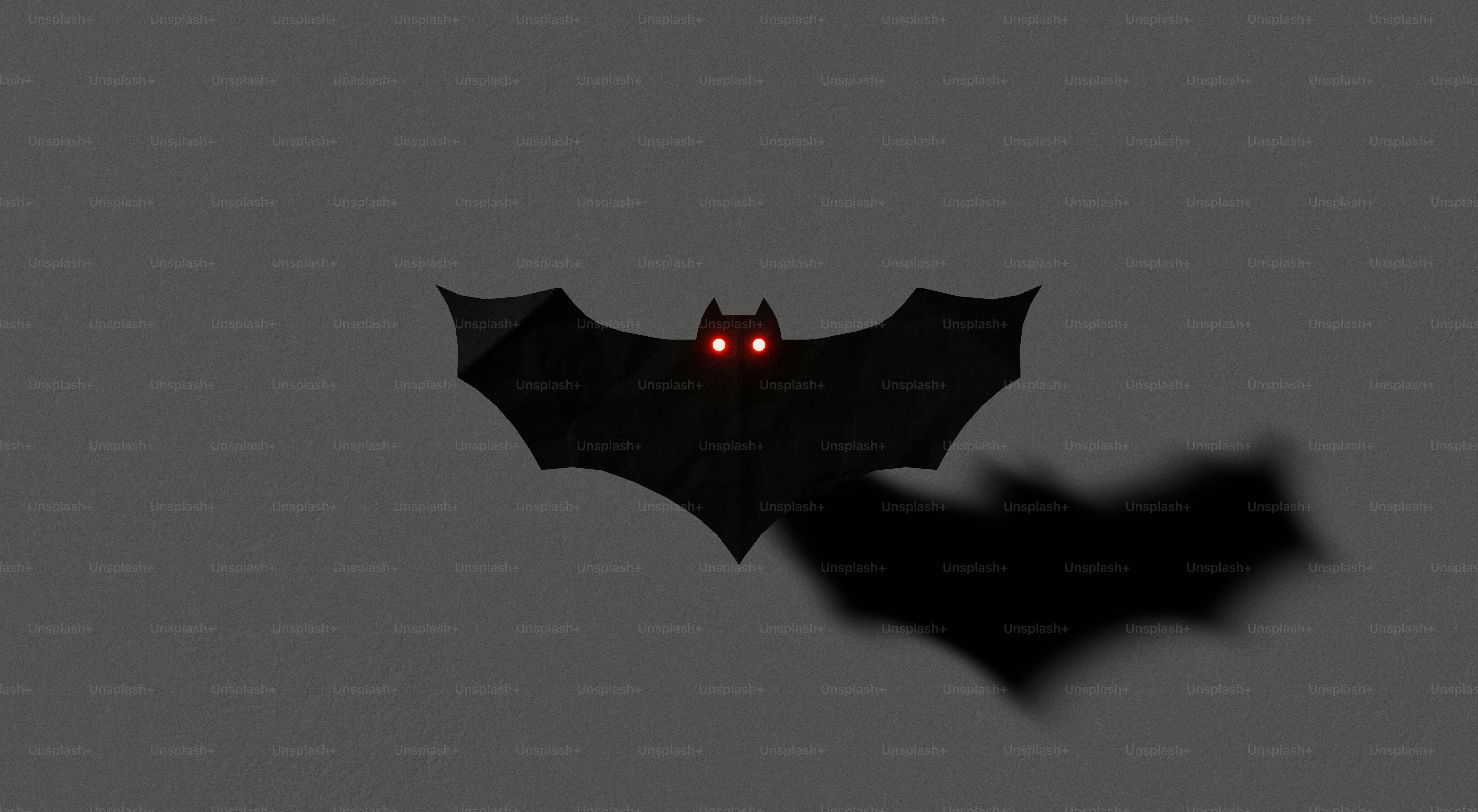 A black bat silhouette with glowing red eyes against a grey wall