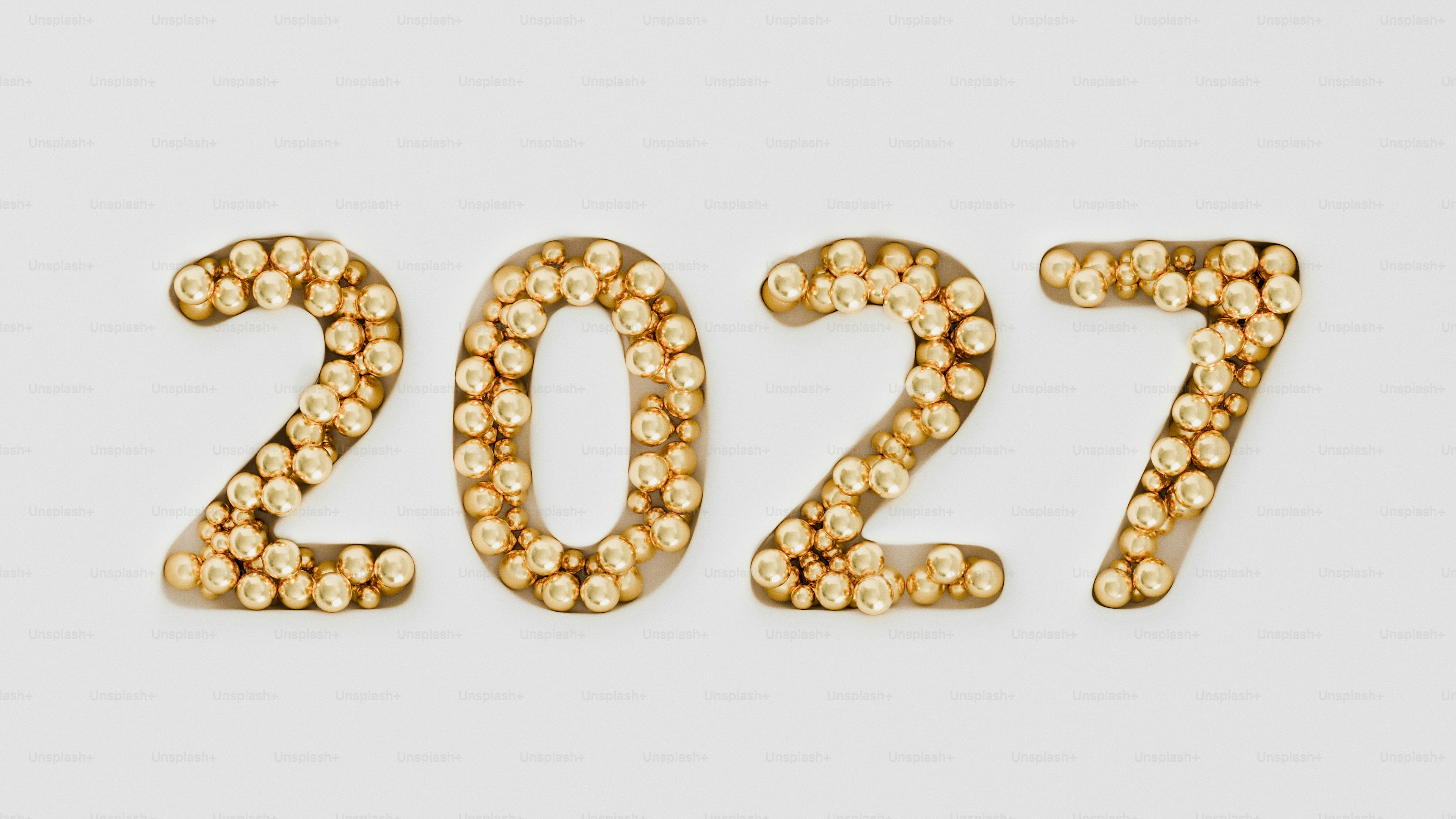 The number 2027 formed by small shiny gold spheres on a white background