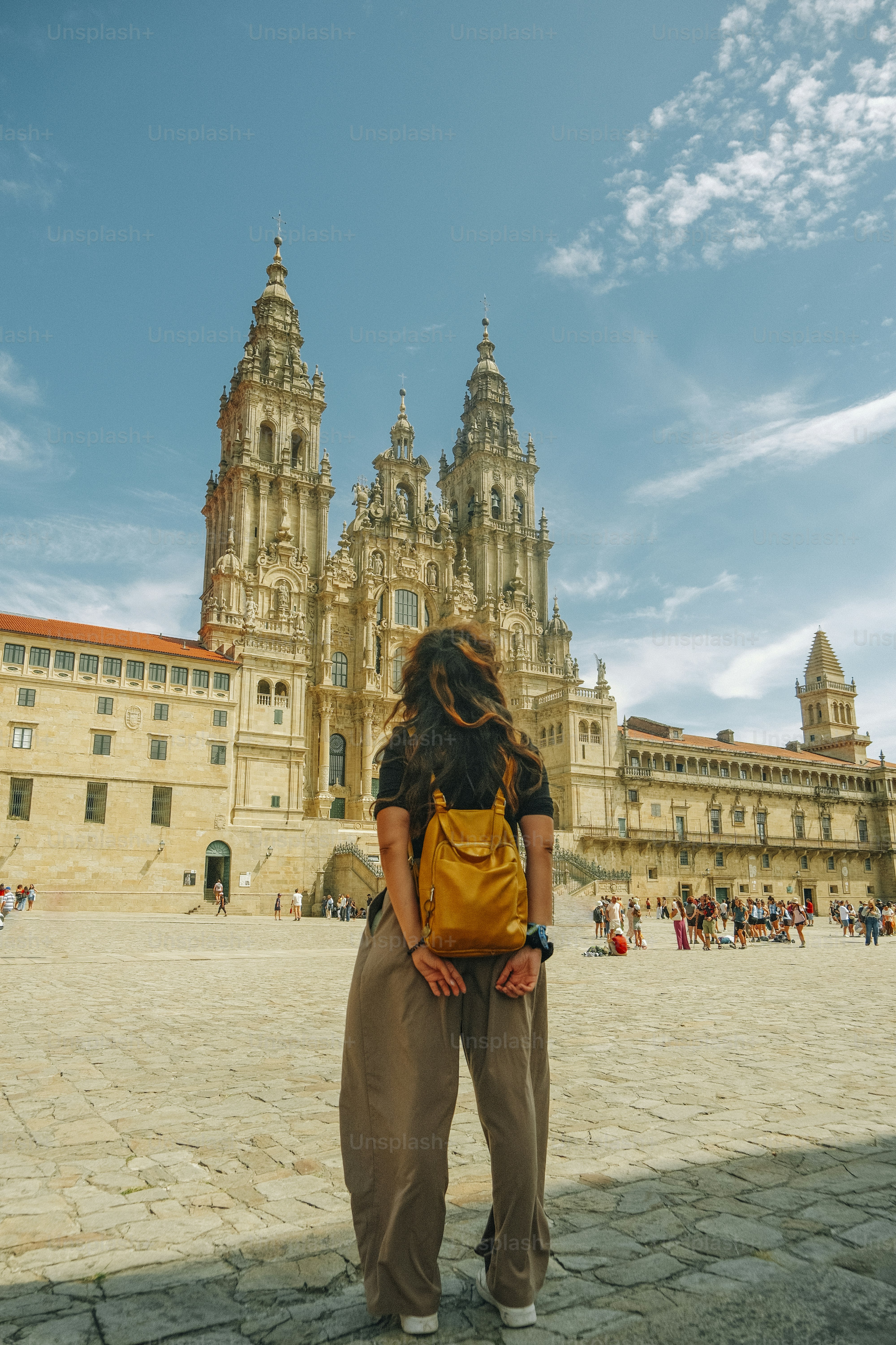 Eine Person mit einem gelben Rucksack blickt auf die Kathedrale von Santiago de Compostela in Spanien