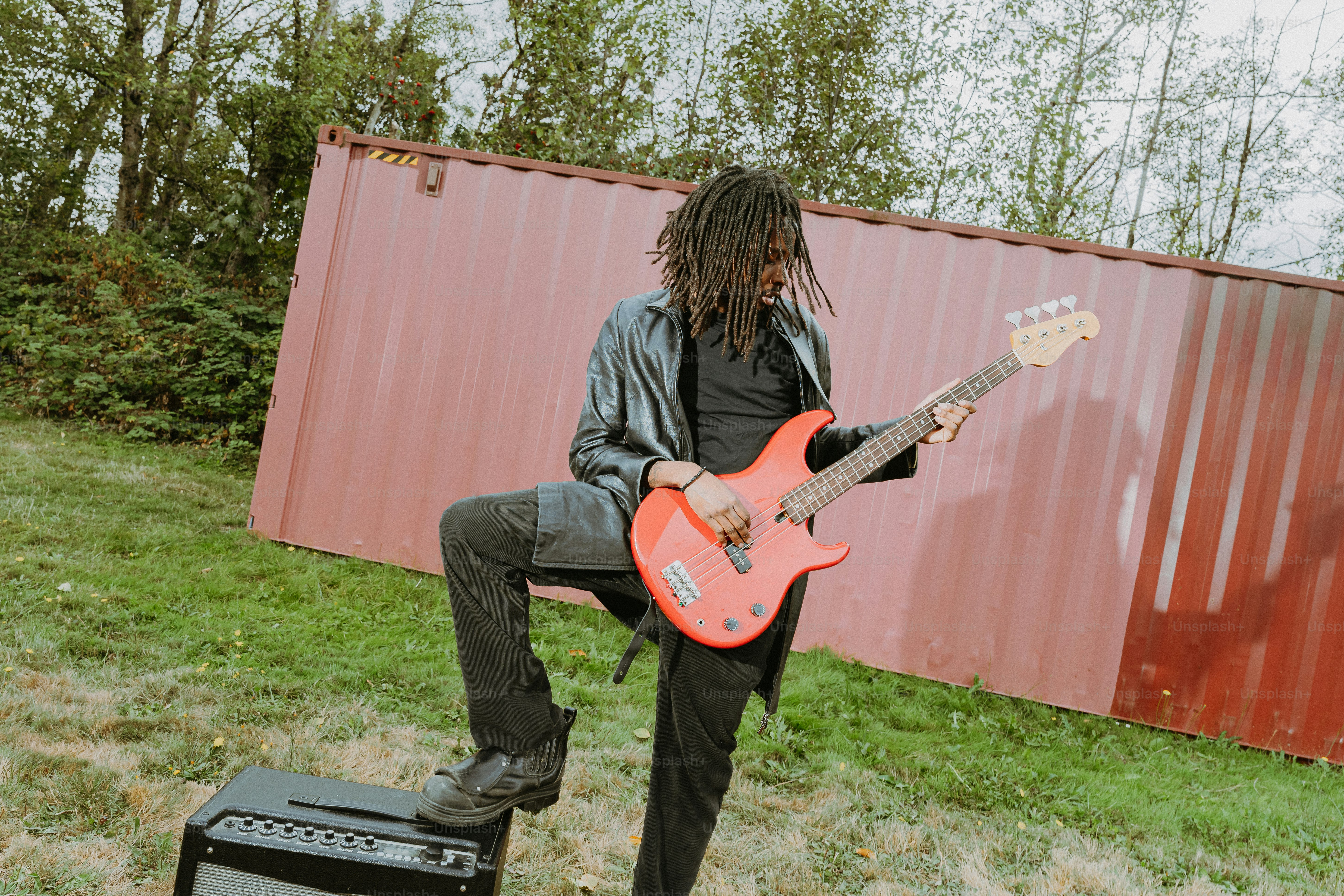 Una persona con i dreadlocks che suona un basso rosso davanti a un container