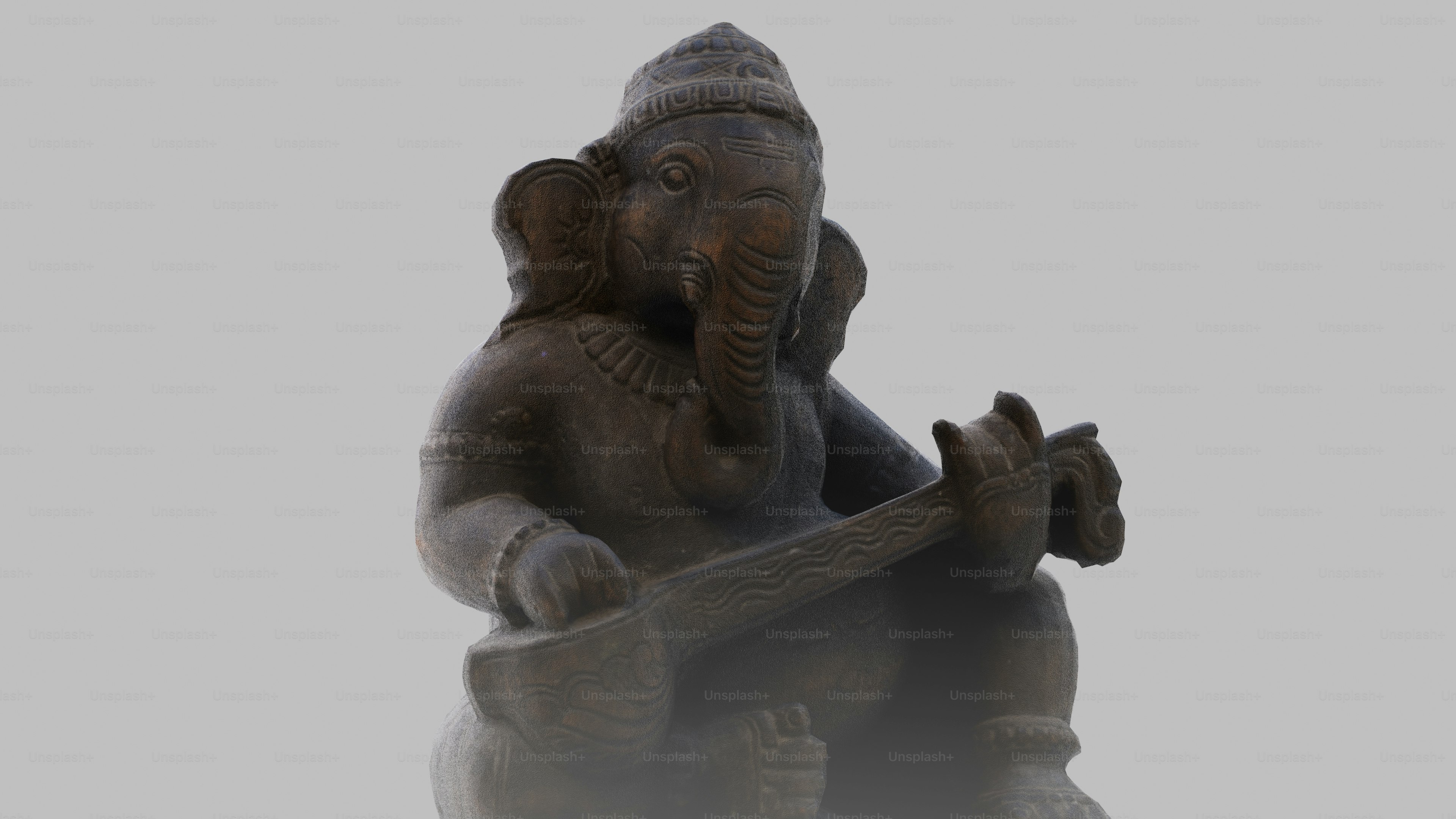 A stone statue of Ganesha playing a stringed instrument against a plain background