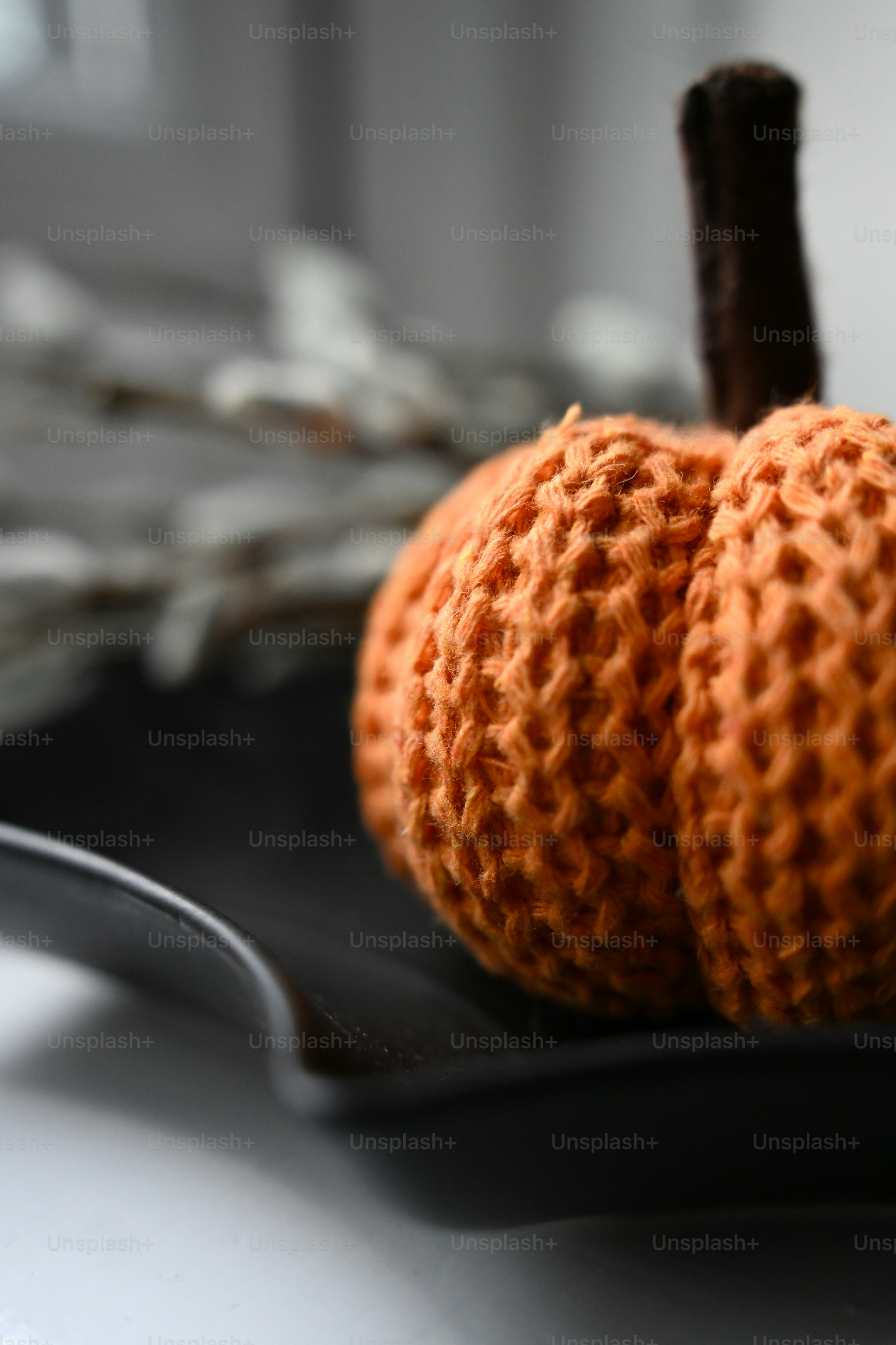 A small orange knitted pumpkin on a black plate with blurred pussy willow branches