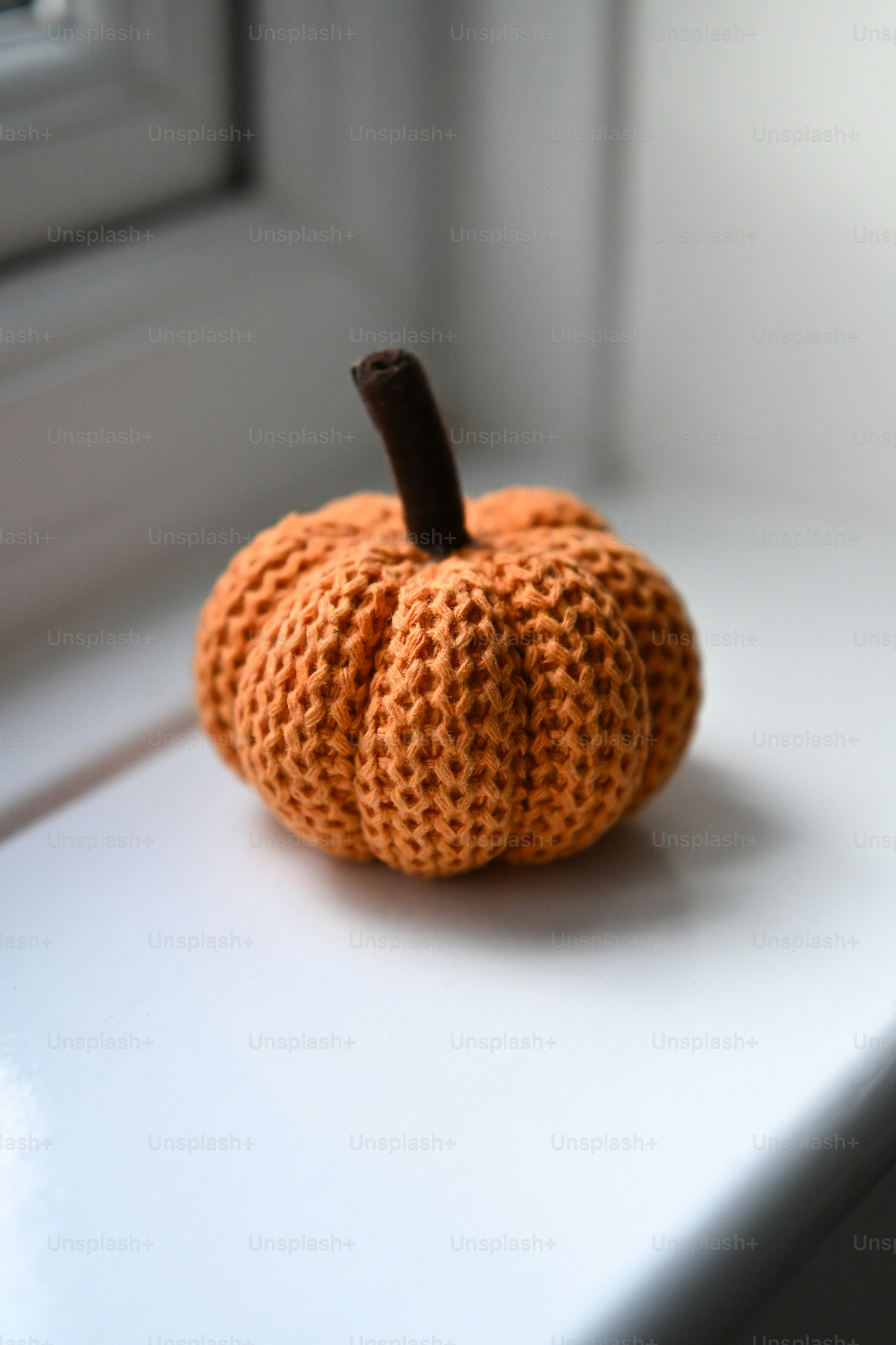 A small orange knitted pumpkin with a brown stem on a white windowsill