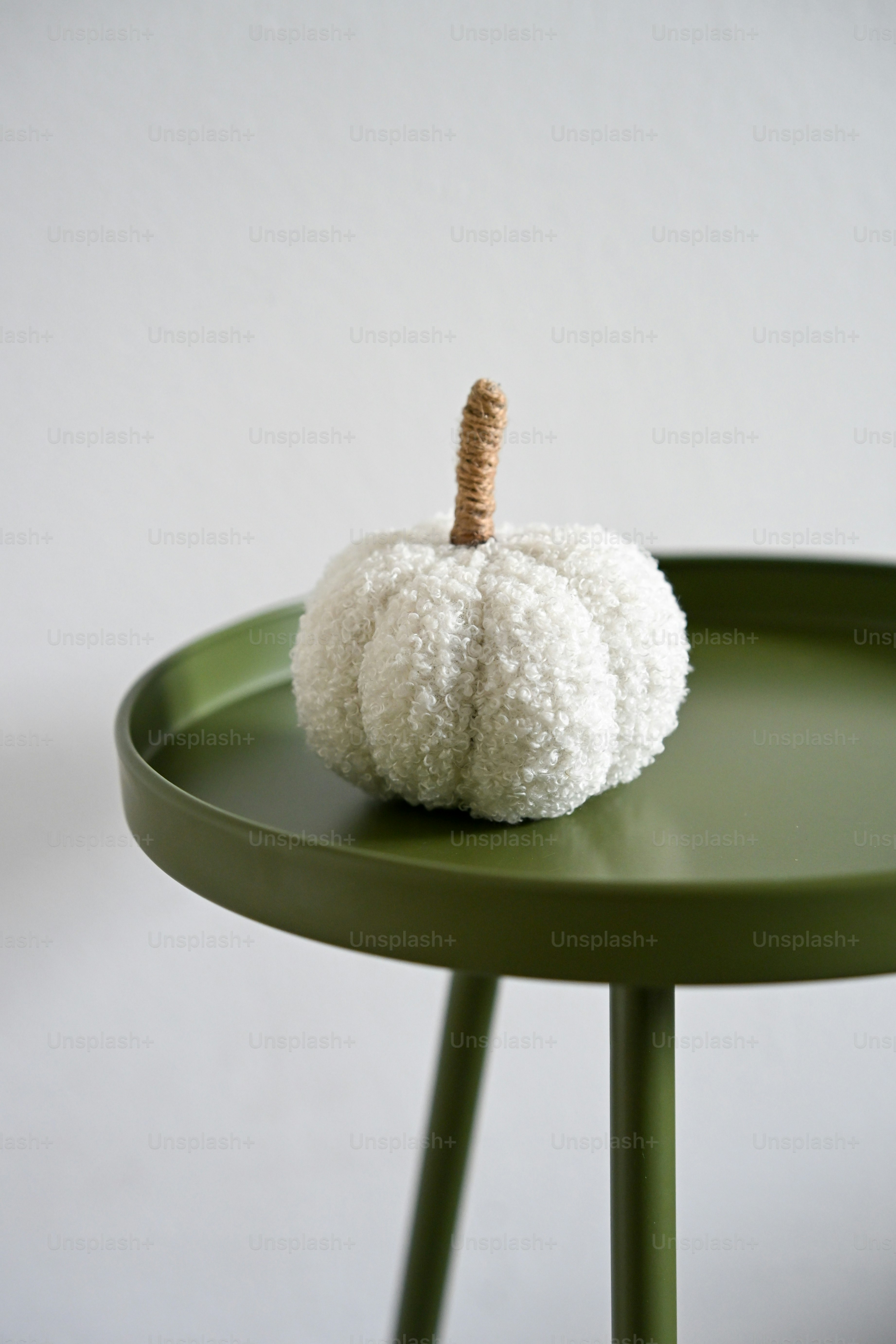 A white textured fabric pumpkin with a twine stem on a green table