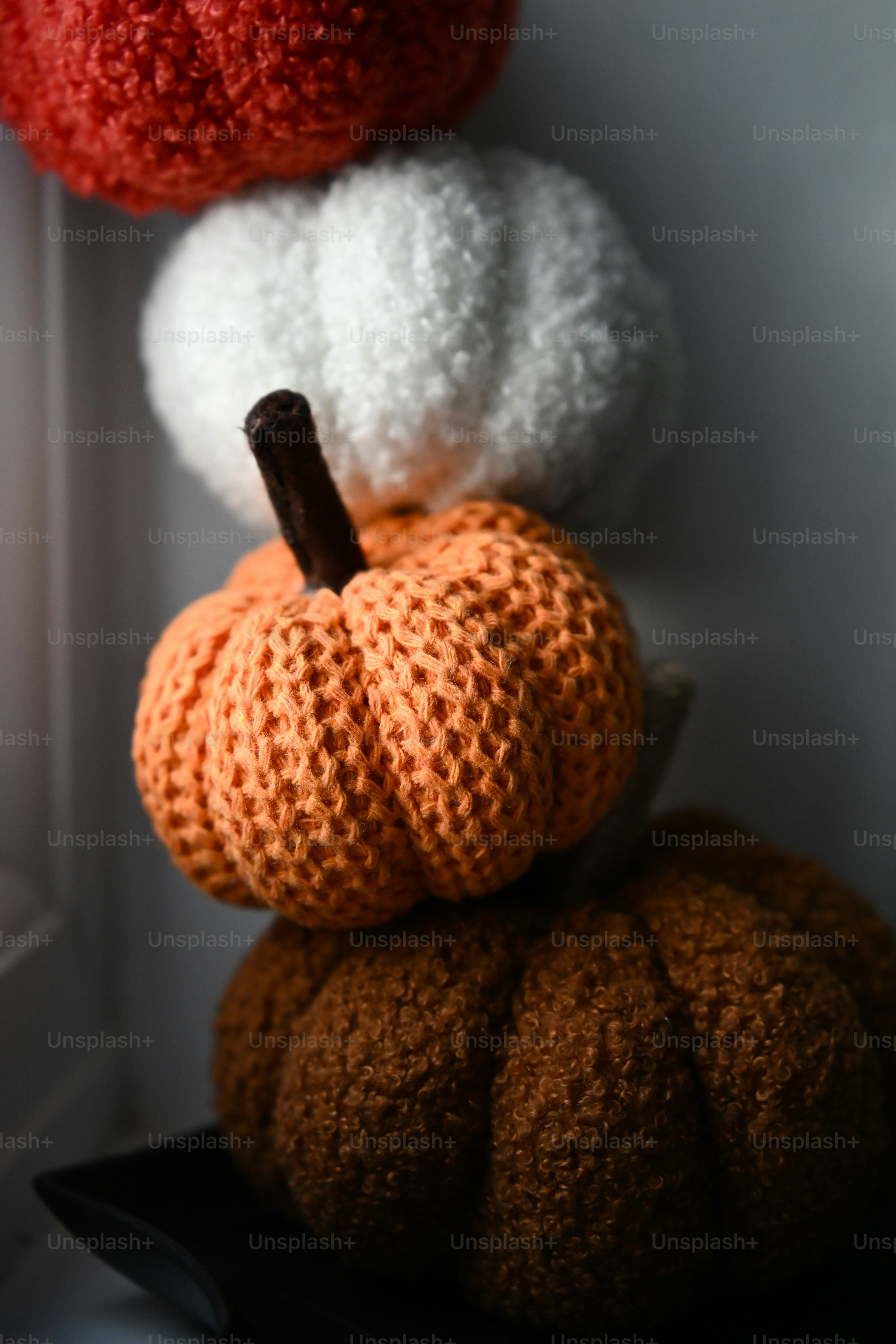 A stack of four knitted pumpkins in red, white, orange, and brown