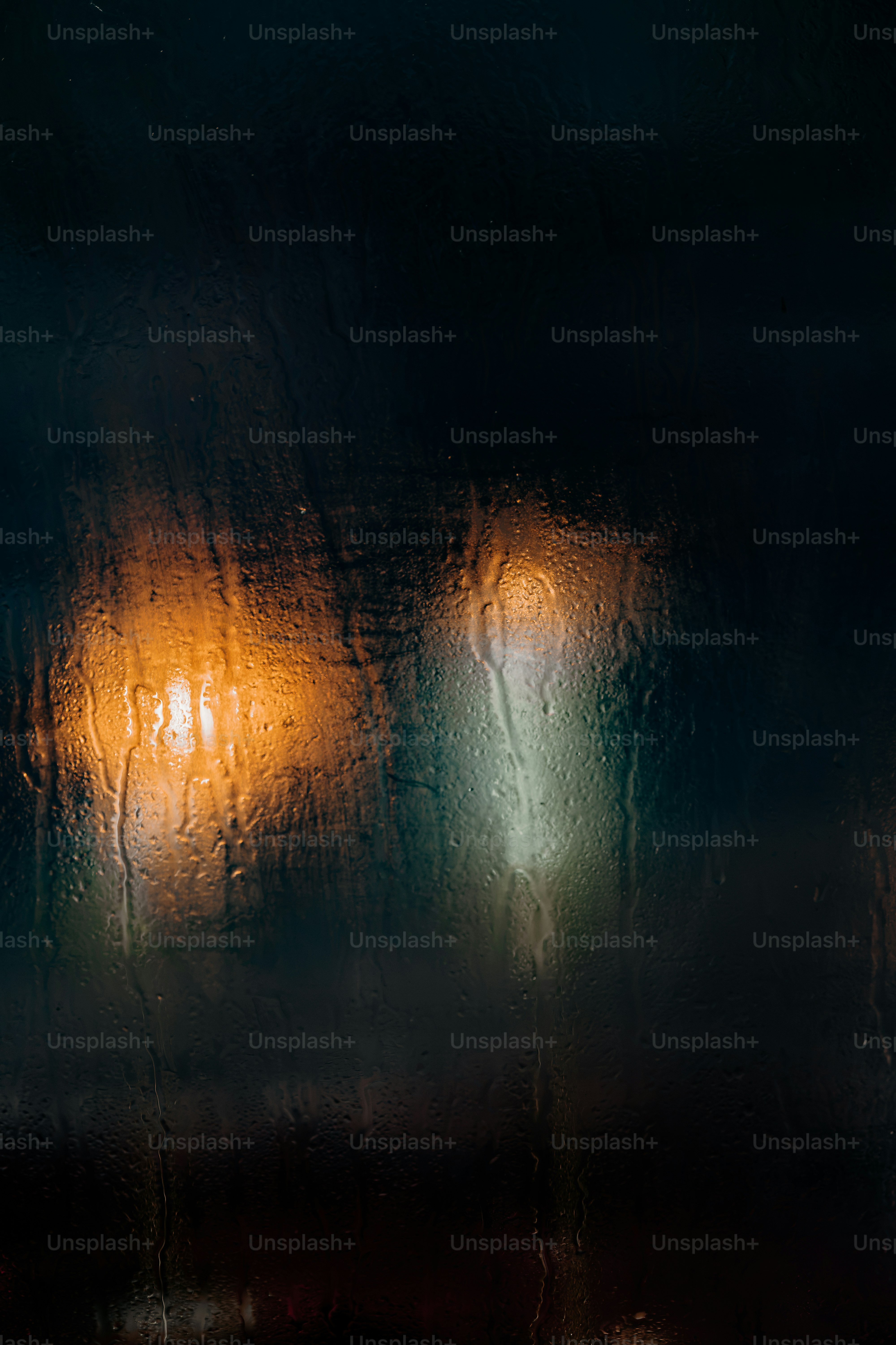 Raindrops on a dark window pane with blurred orange and white city lights