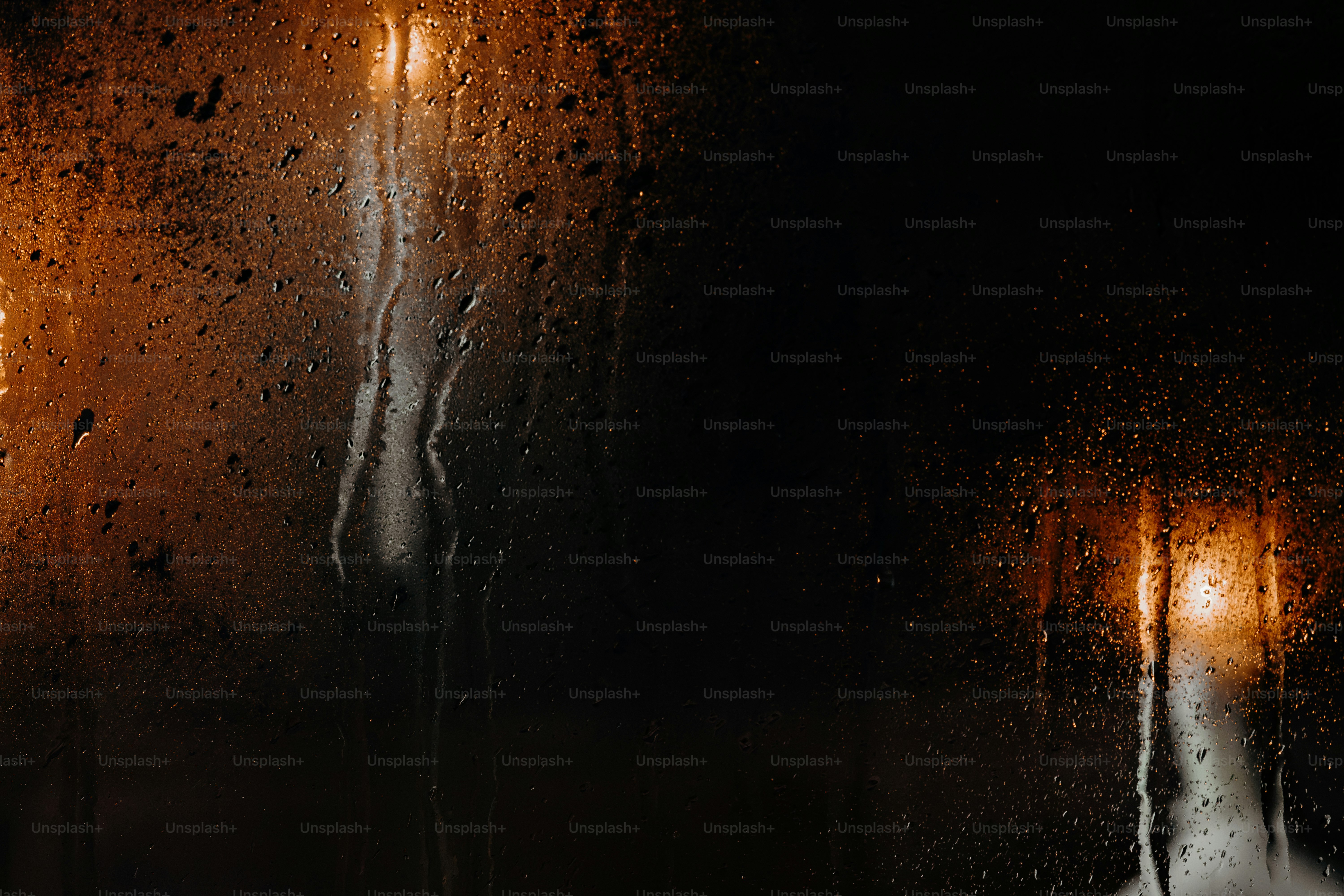 Raindrops on a dark window pane illuminated by warm golden light