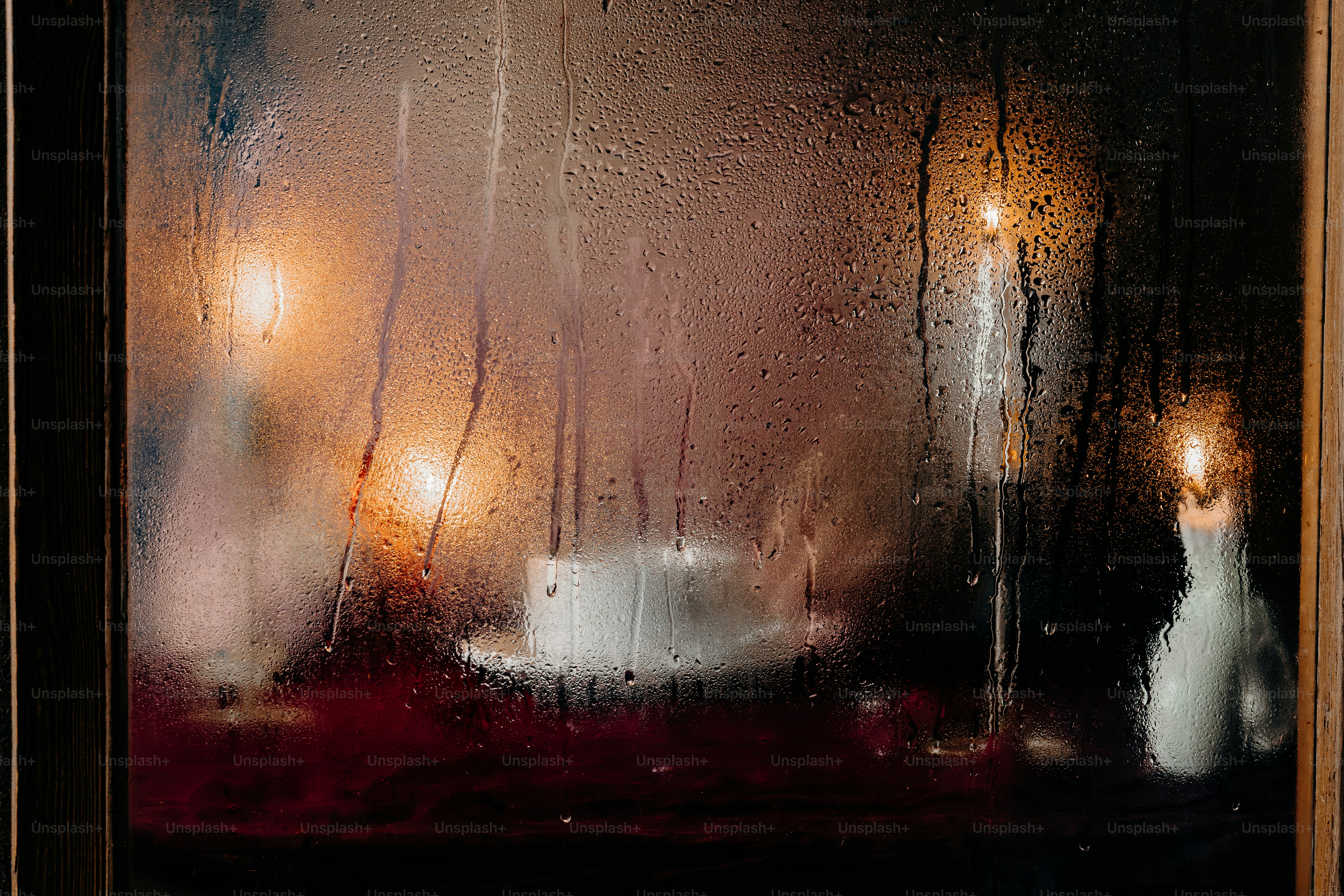 Raindrops on a window pane with warm candlelight glowing in the dark interior