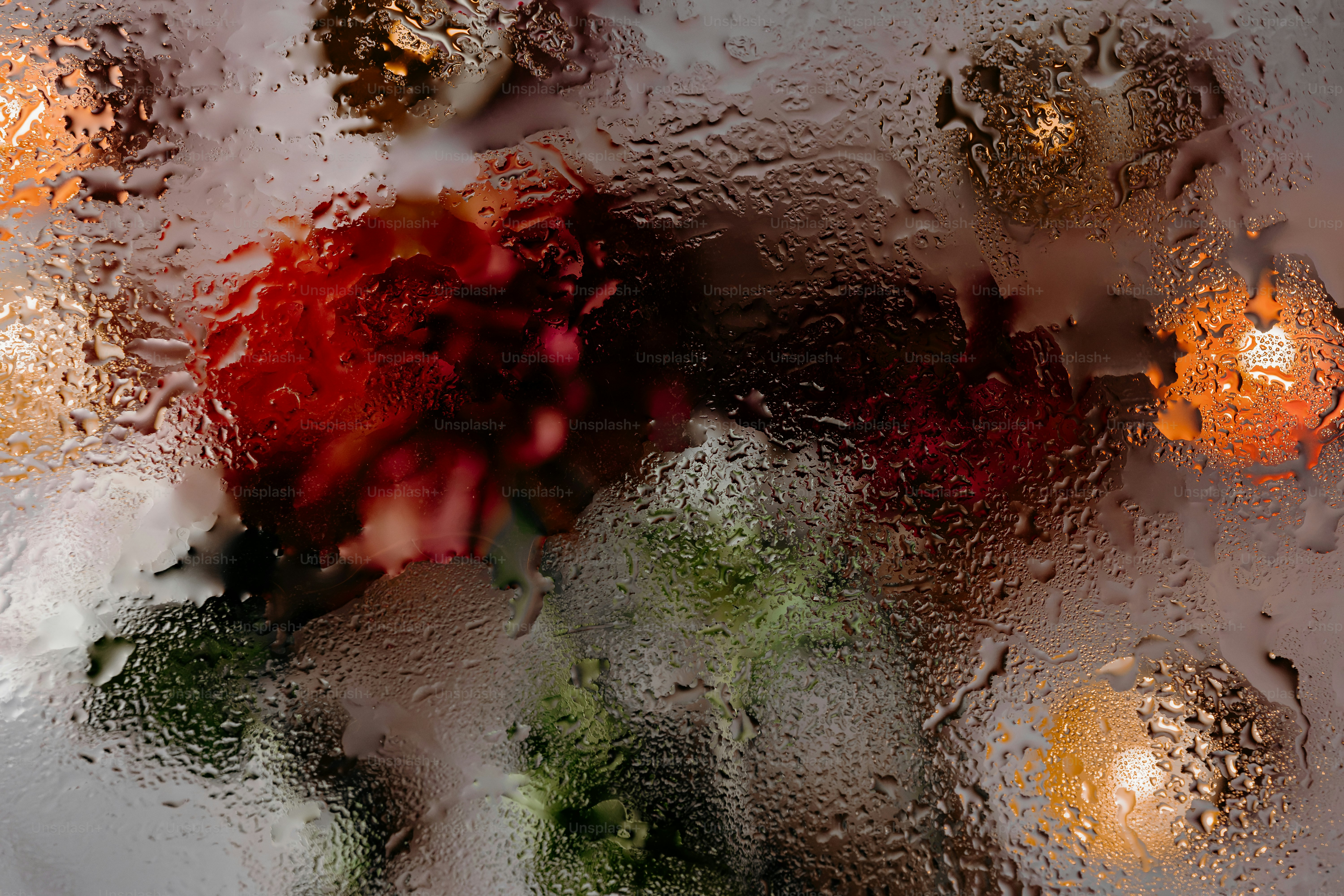 Raindrops on a window pane obscuring a bouquet of red flowers and warm lights