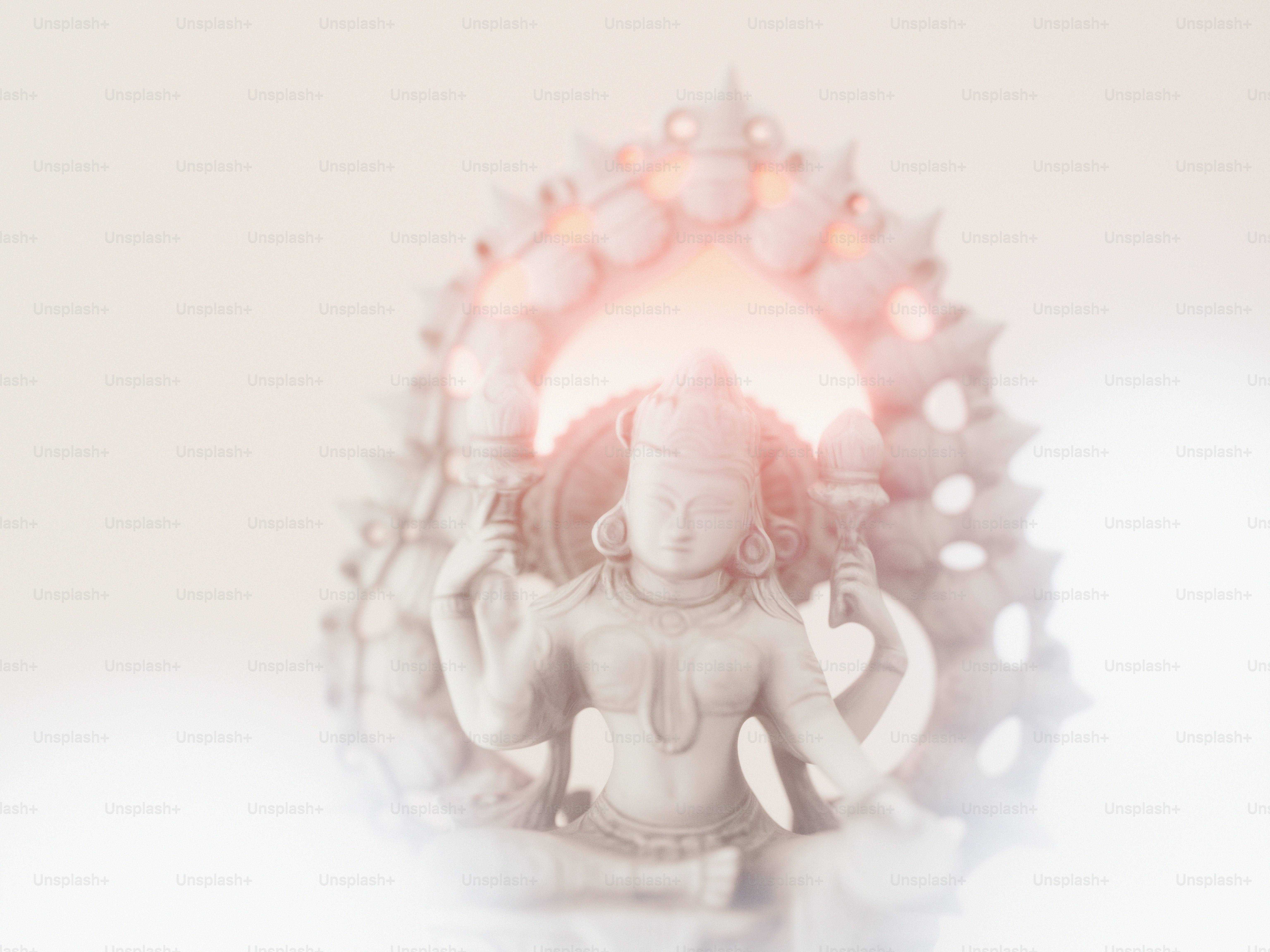 A white stone statue of a deity with multiple arms in a soft glow