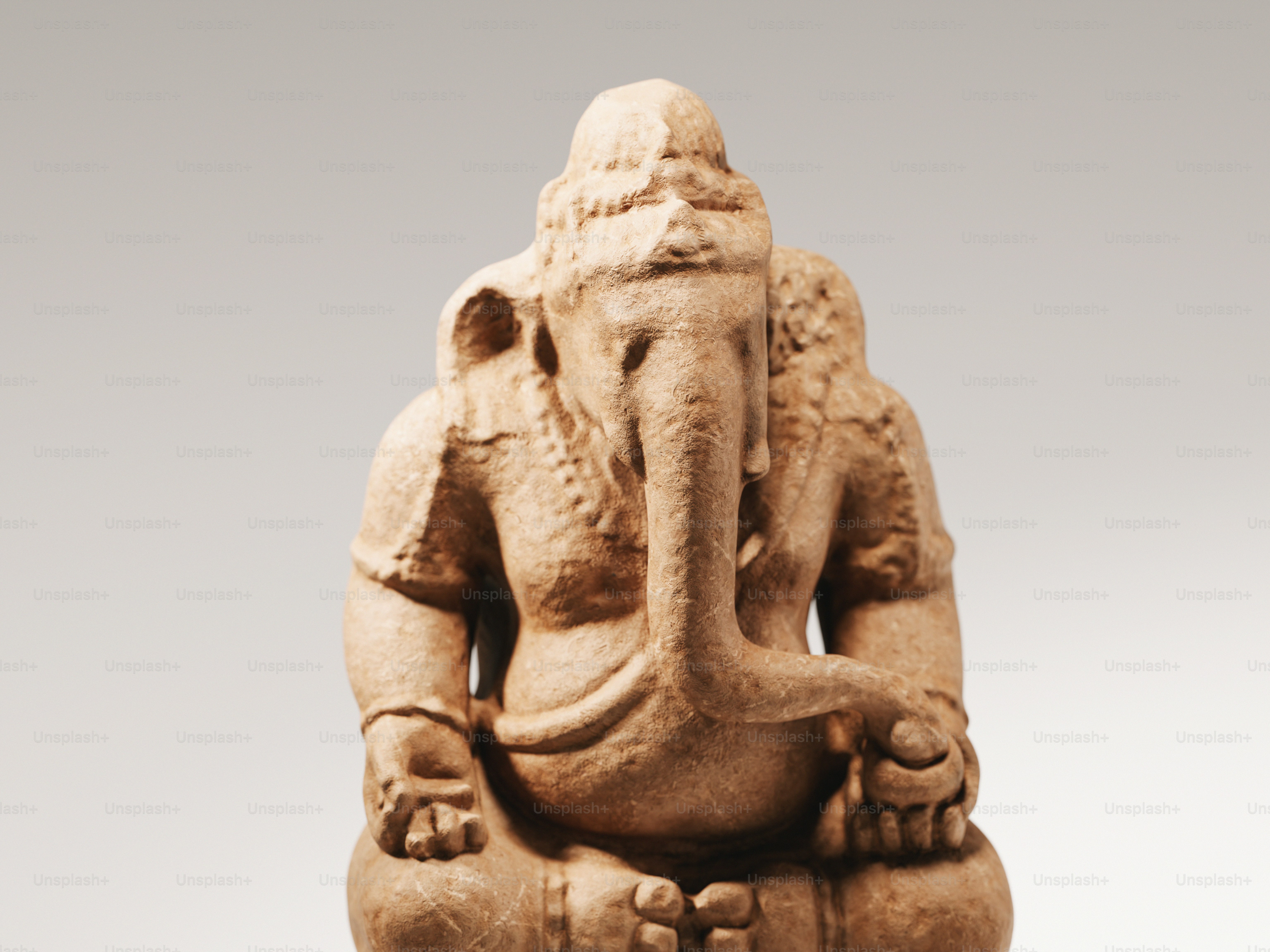 A terracotta statue of Ganesha sitting in a meditative pose against a plain background