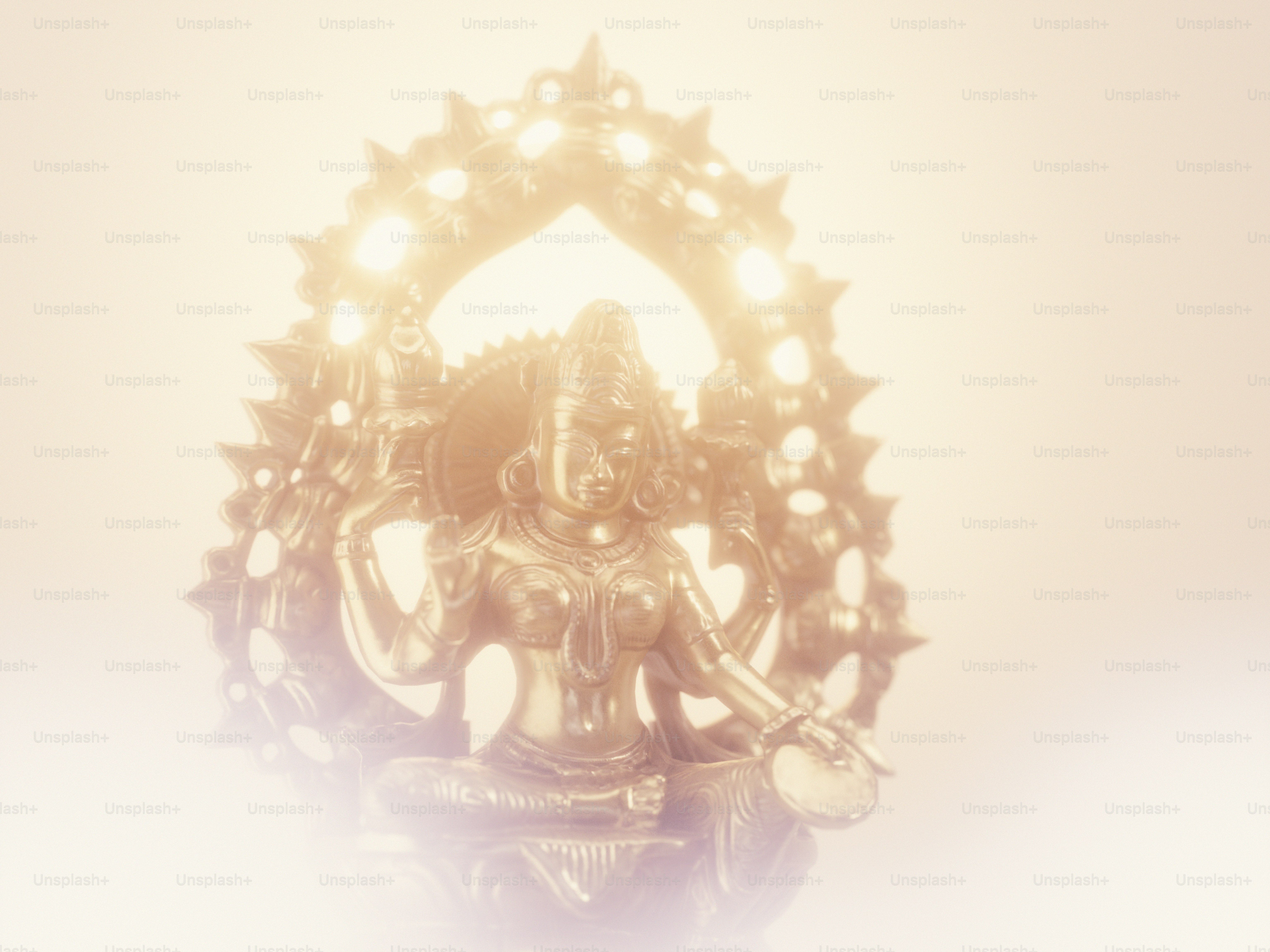 A golden statue of a deity with multiple arms against a bright background