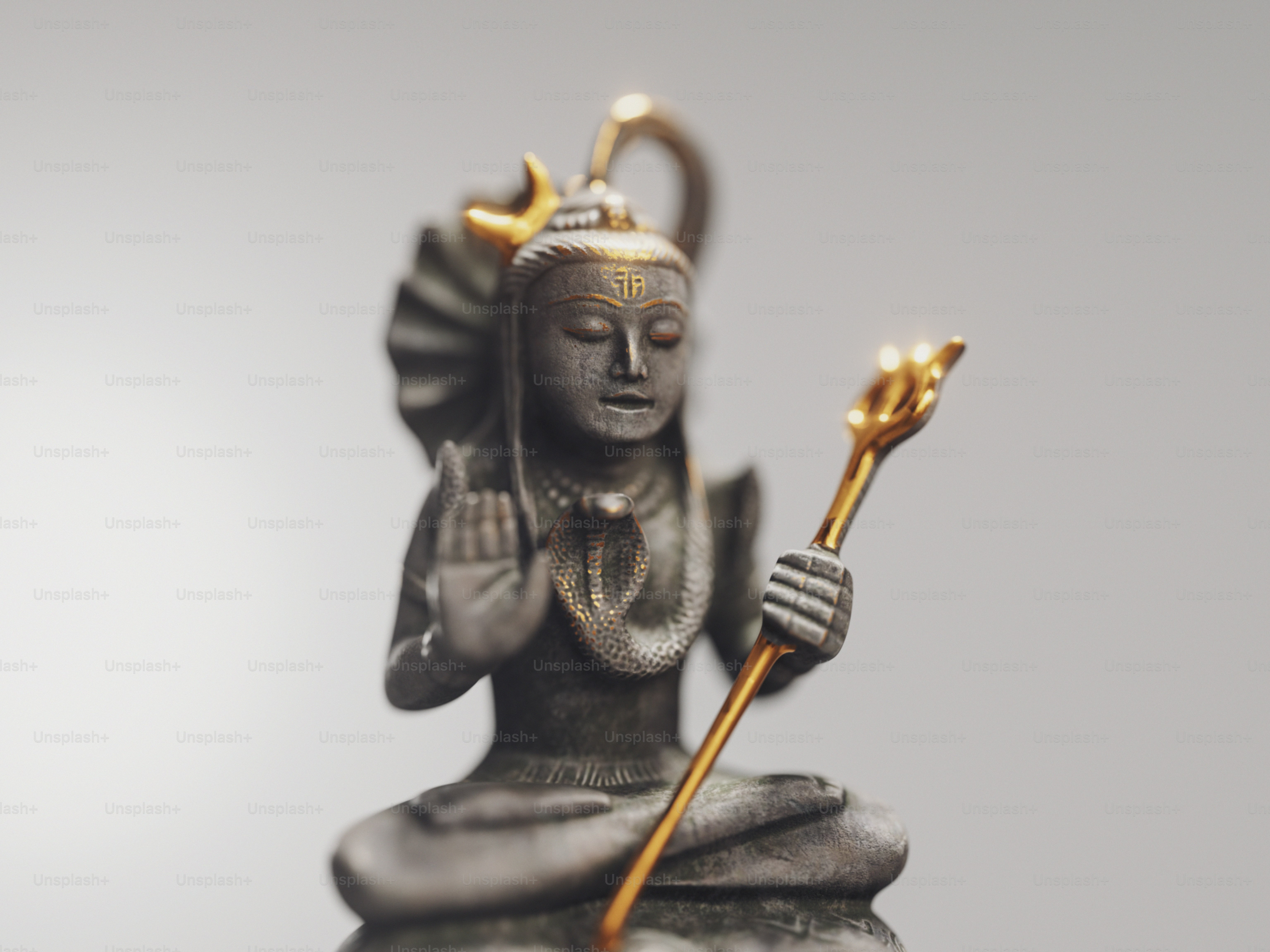 A grey stone statue of Shiva with gold accents holding a trident