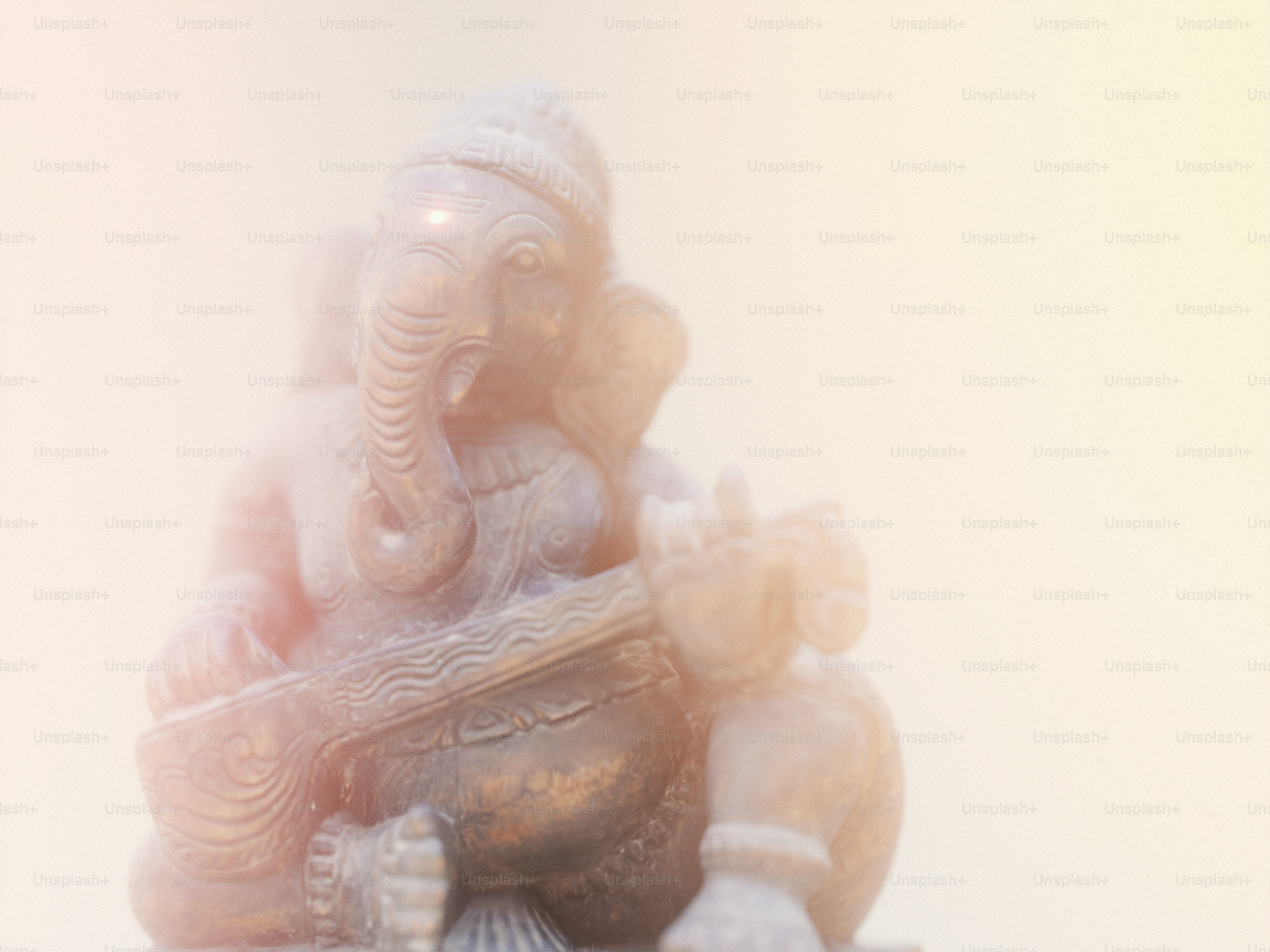A stone statue of Ganesha playing a veena in soft golden light