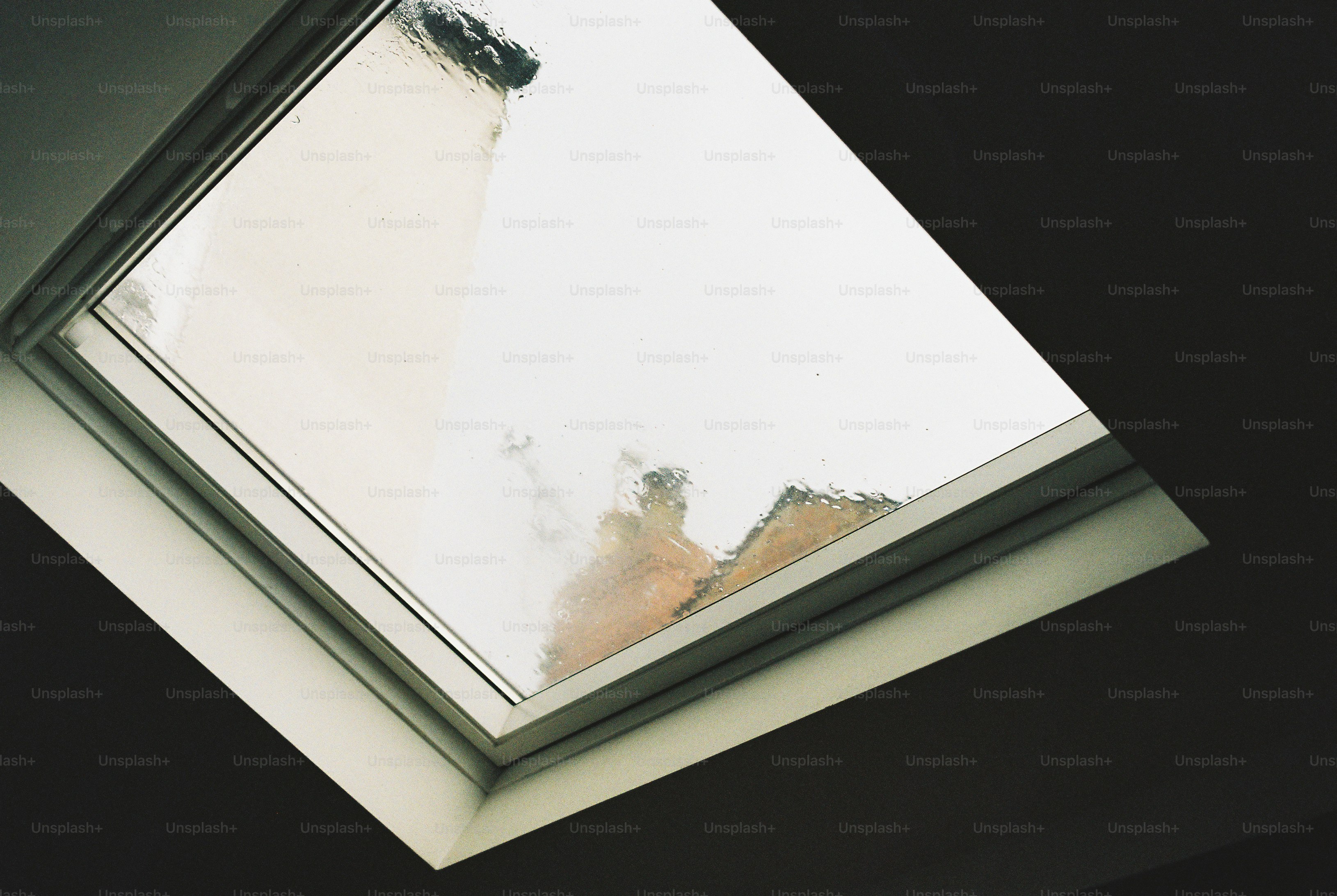 Raindrops on a square skylight window with a view of a building roof