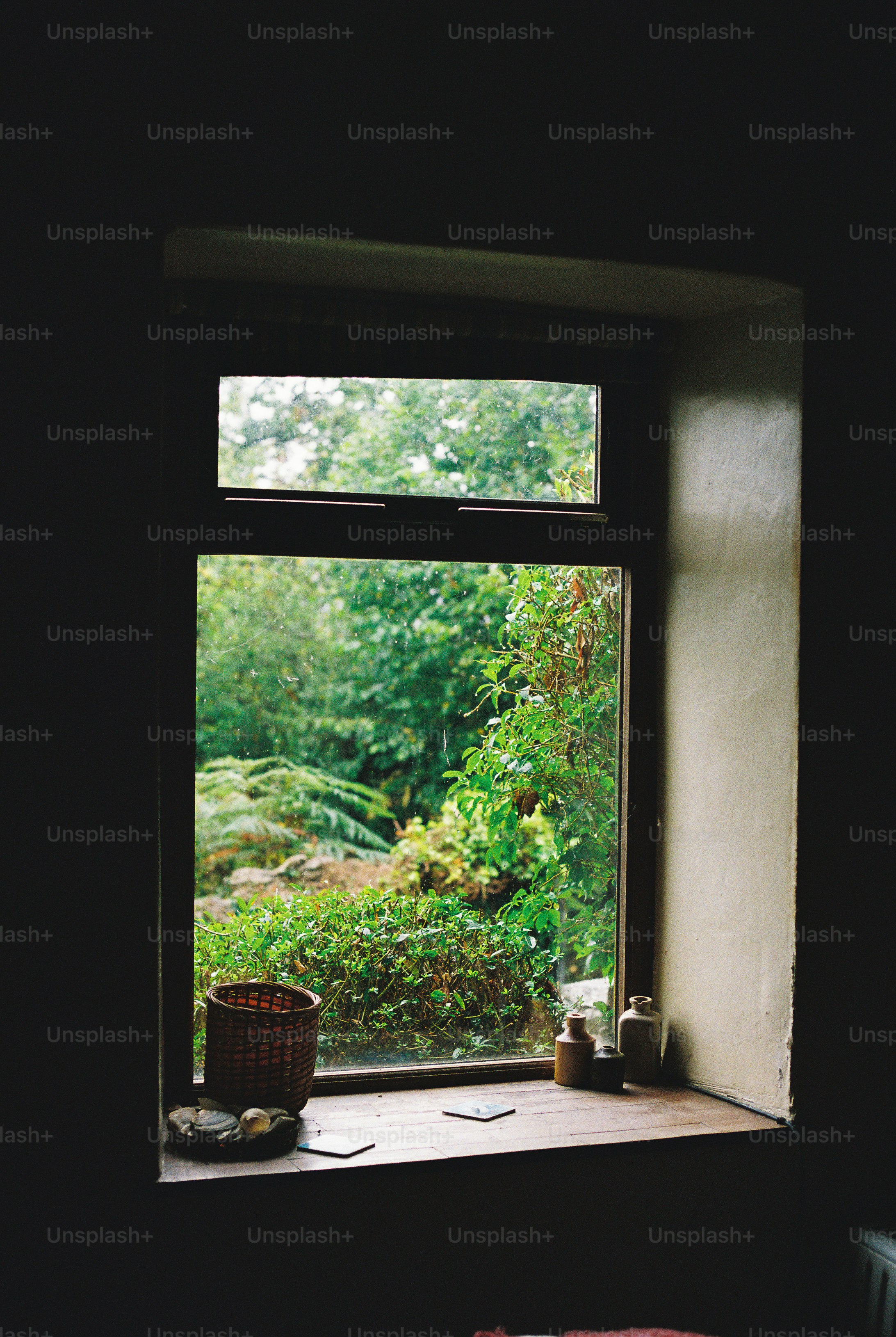 A wooden window sill with a woven basket and small ceramic bottles overlooking greenery
