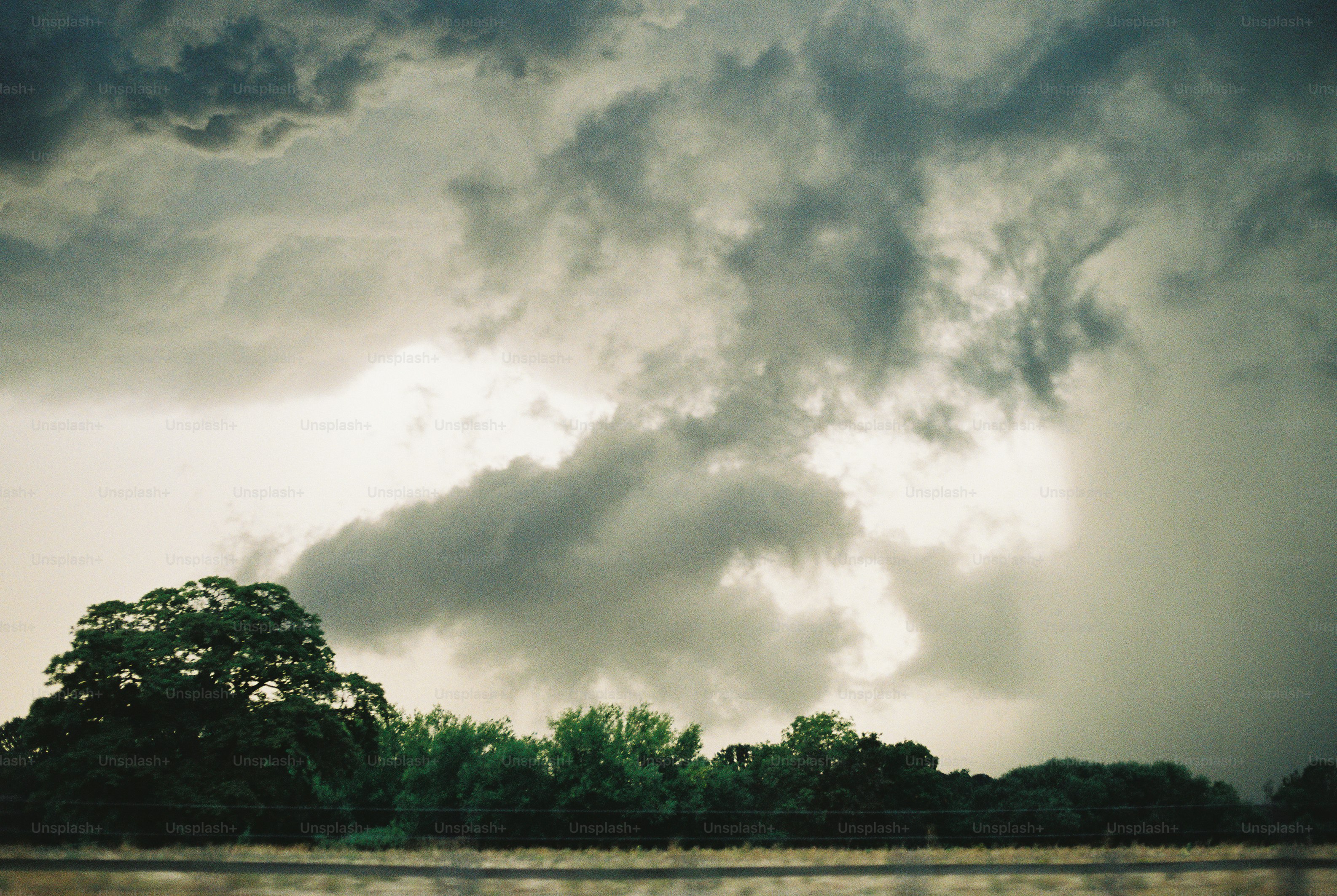 Nubes oscuras de tormenta que se forman sobre una línea de árboles verdes en un campo