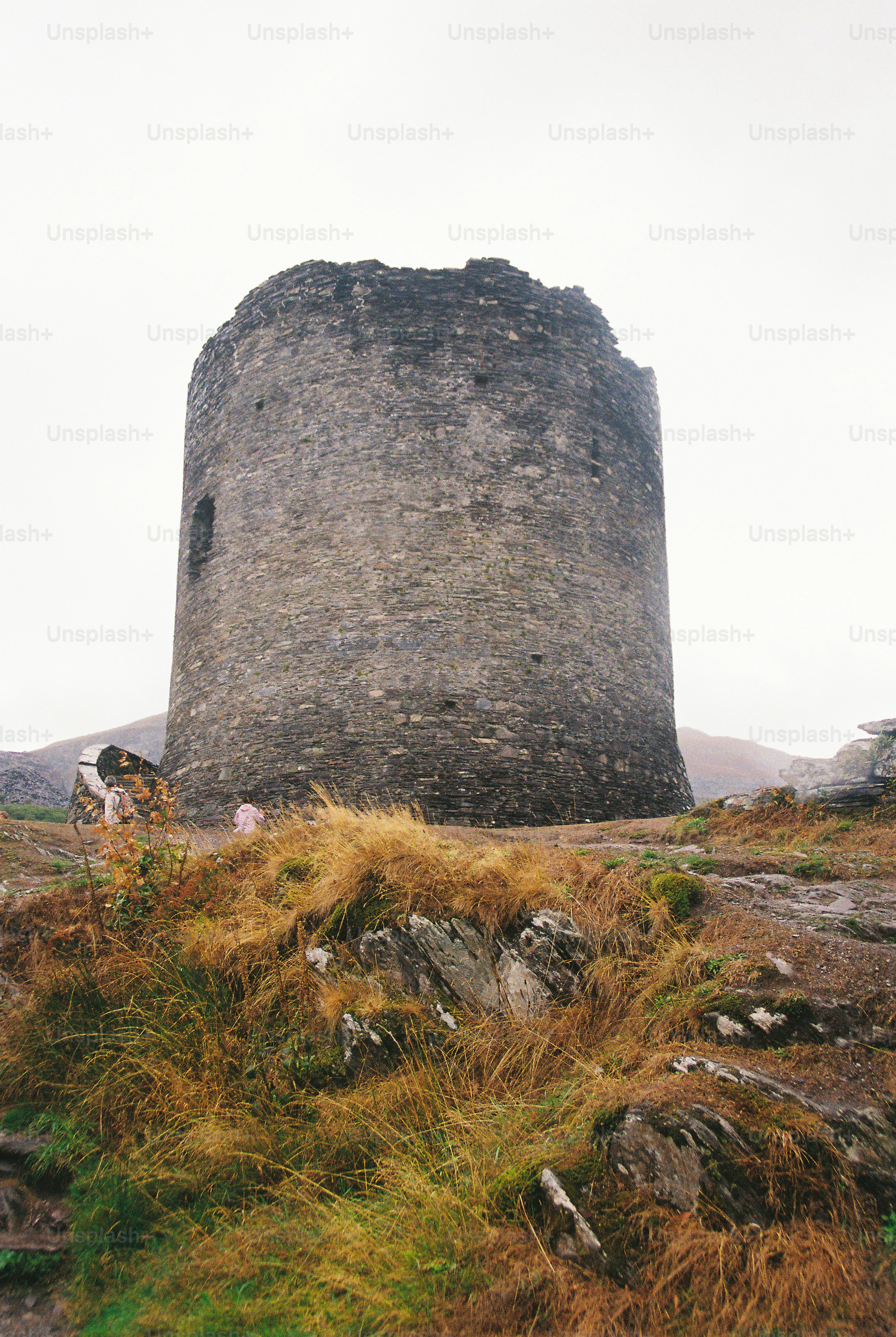 A tall cylindrical stone tower on a grassy hill under an overcast sky