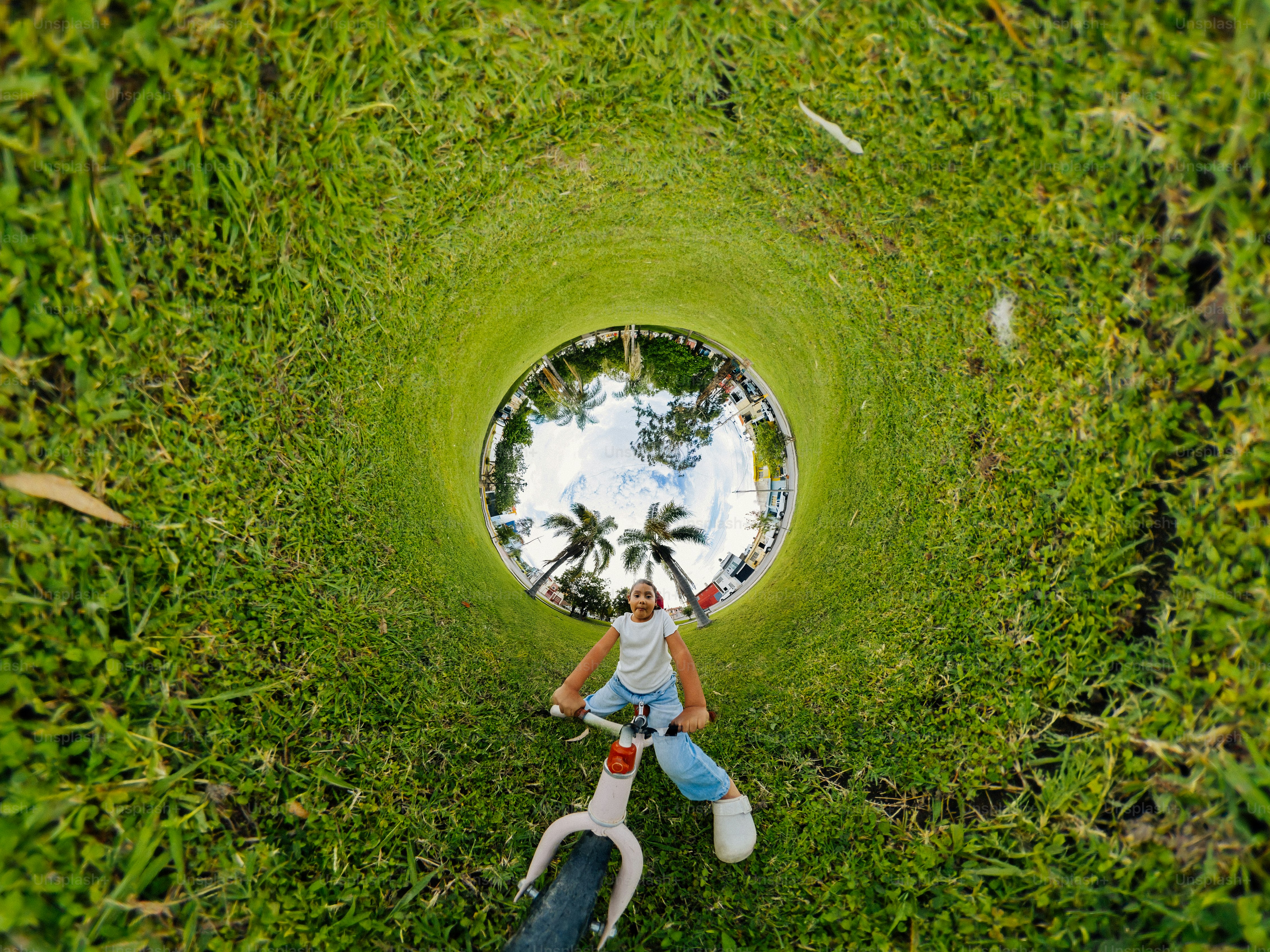 A child cycling on a grass field in a distorted 360 degree panoramic view