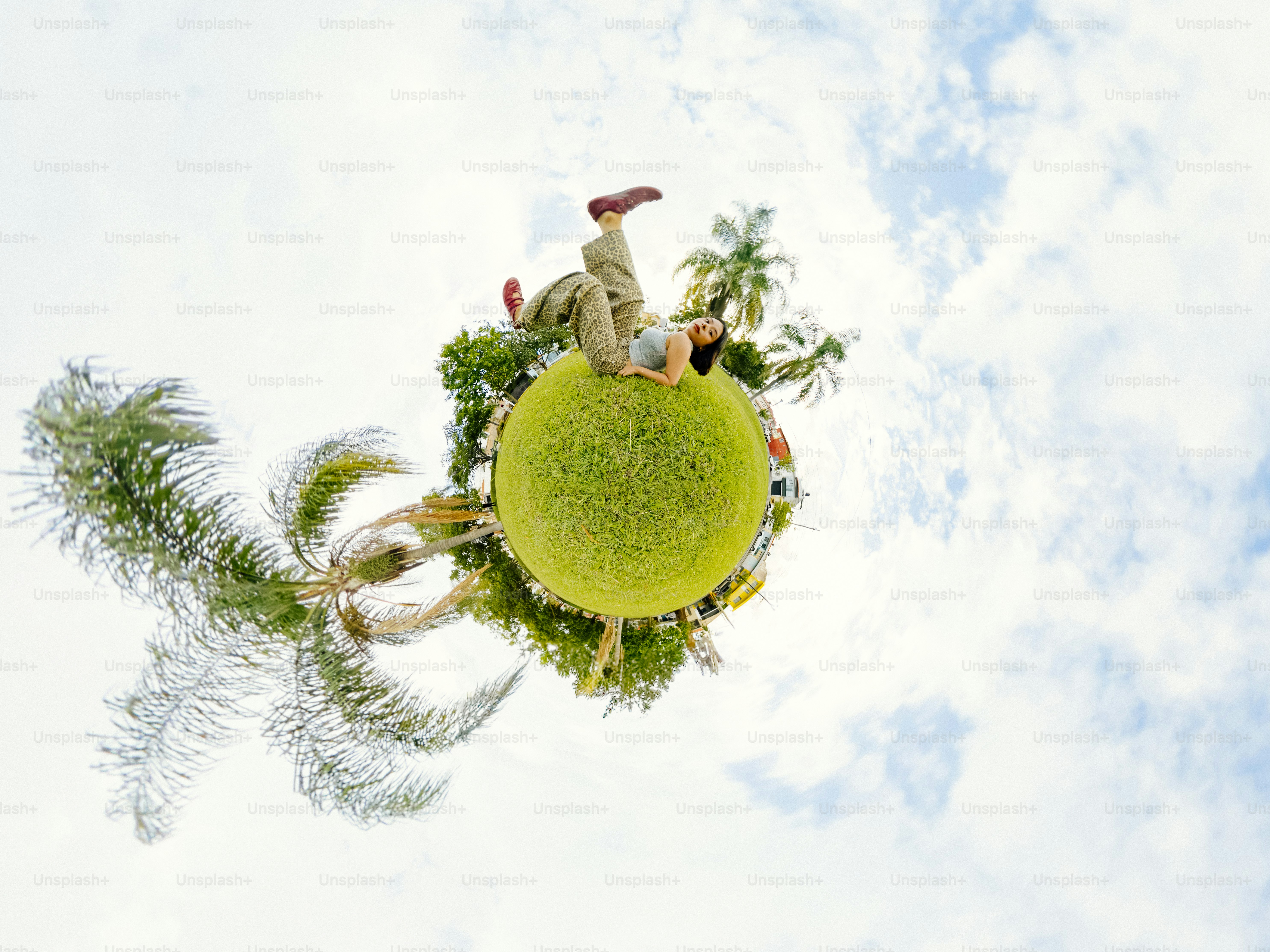 A woman lying on a small grassy planet with palm trees under a cloudy sky
