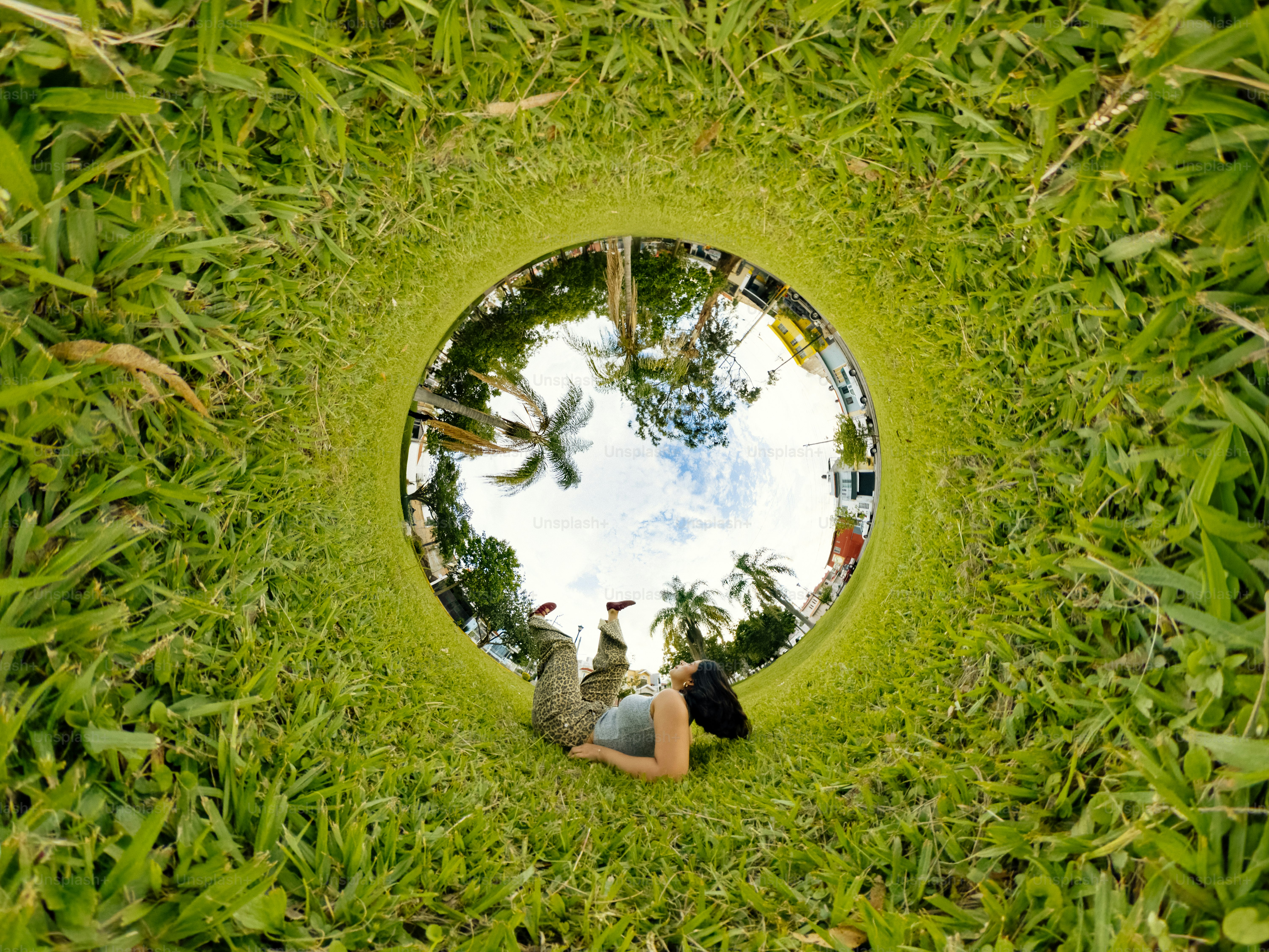 A person lying on green grass in a circular panoramic view of a park