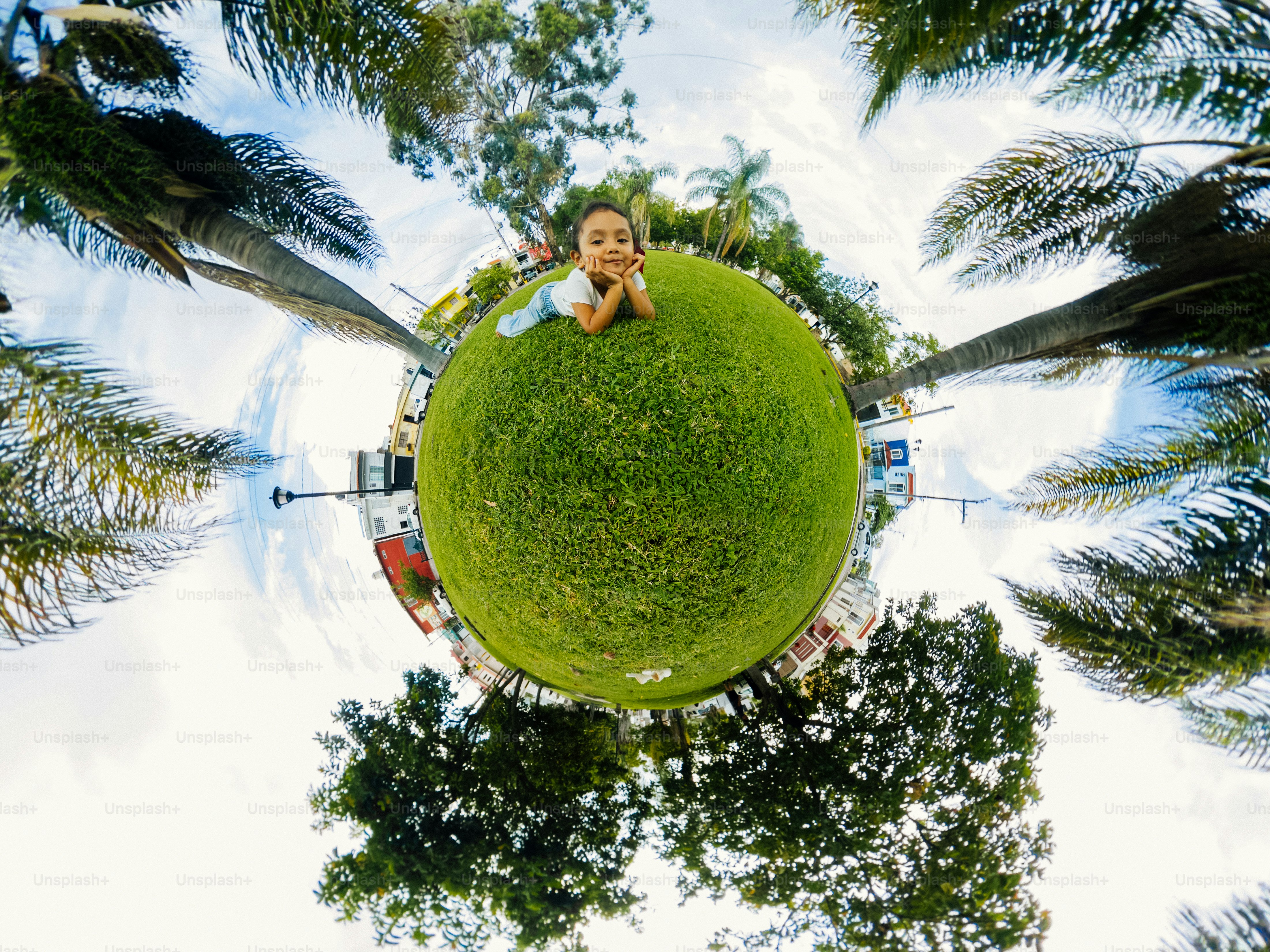 A child lying on a circular patch of green grass surrounded by palm trees