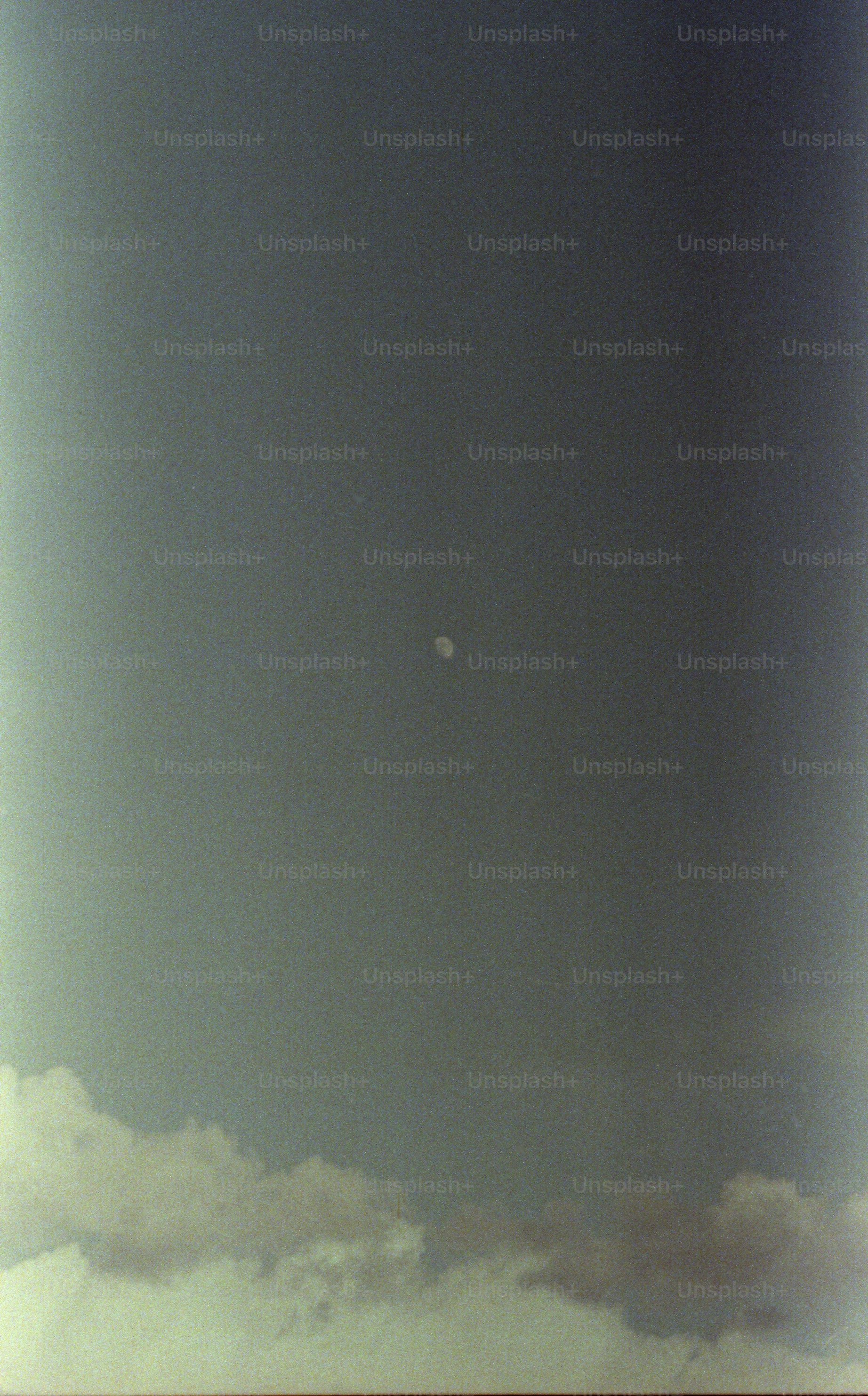 A small moon visible in a dark grey sky above low clouds