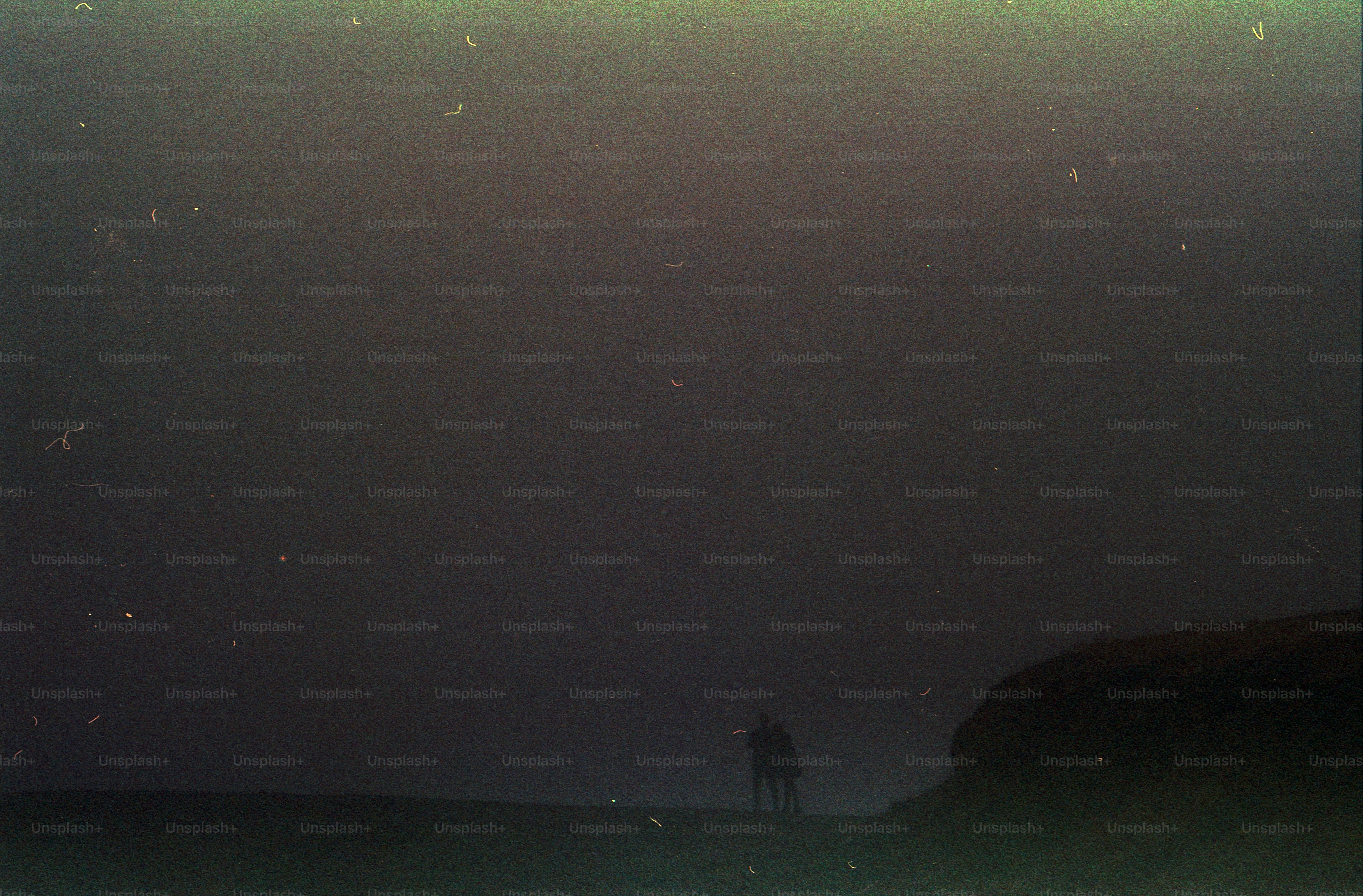 Two people in silhouette against a dark, grainy sky on a horizon line