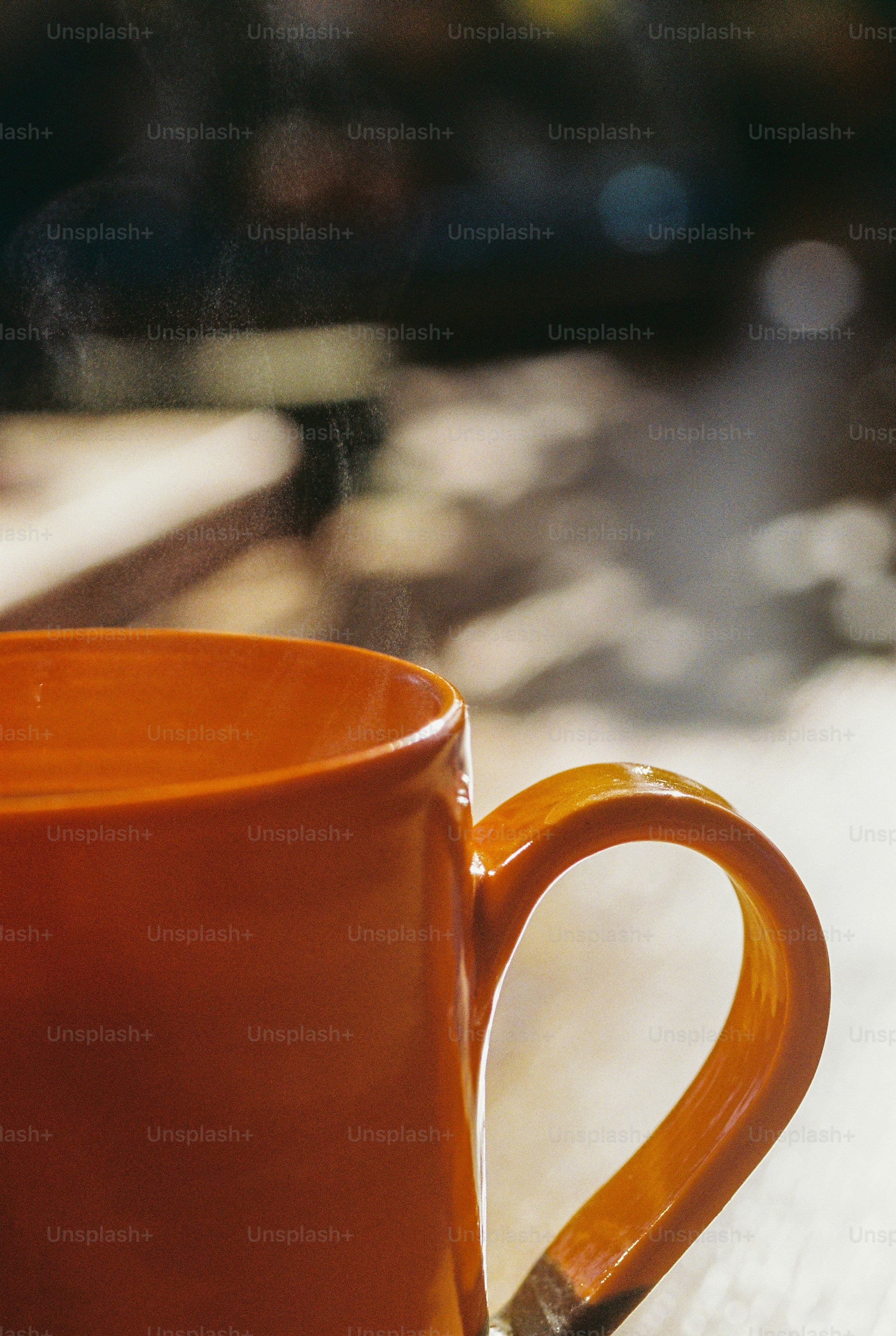 A steaming orange coffee mug on a table in warm sunlight