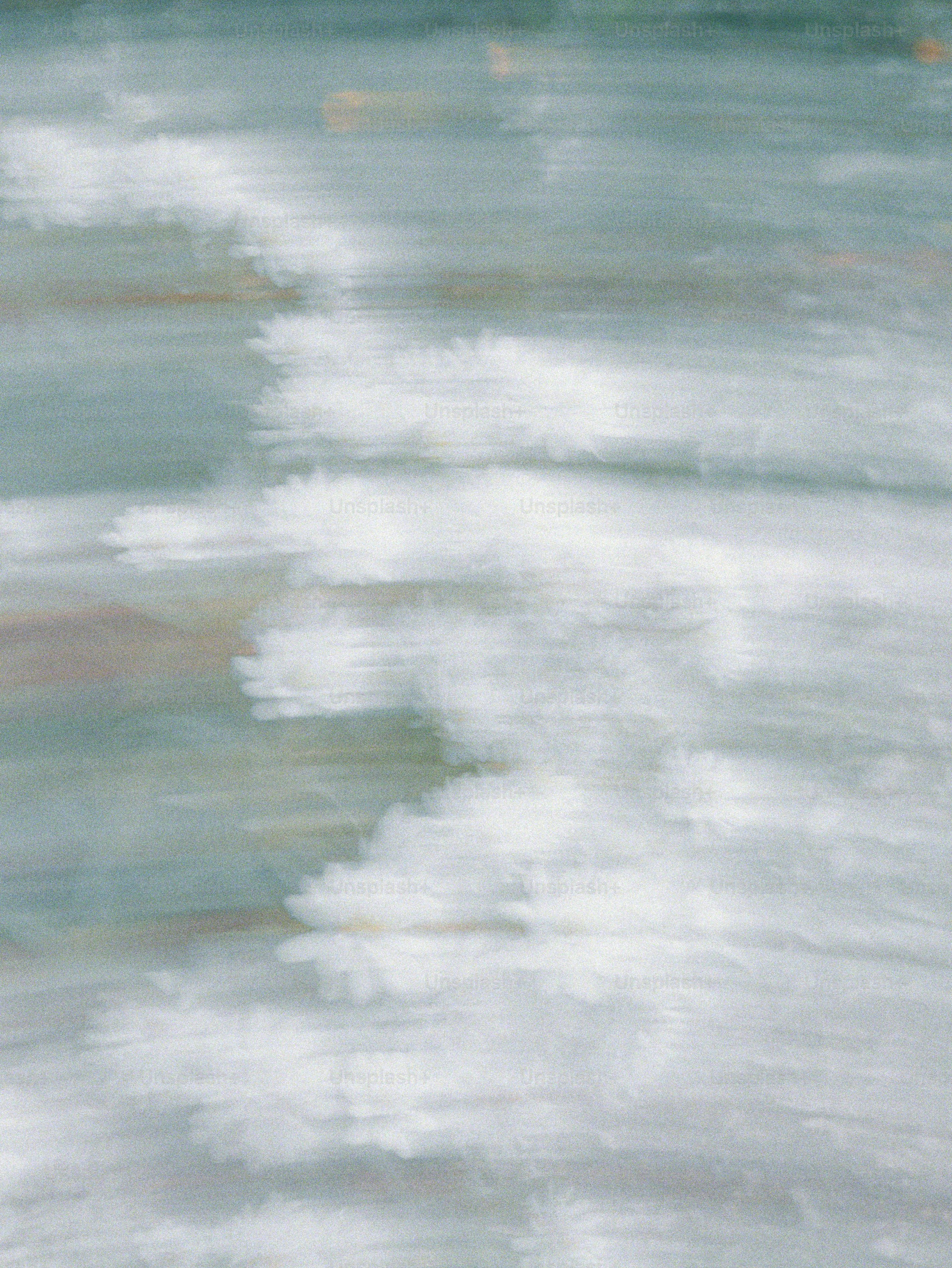 Blurred white sea foam moving across a calm blue and green ocean surface