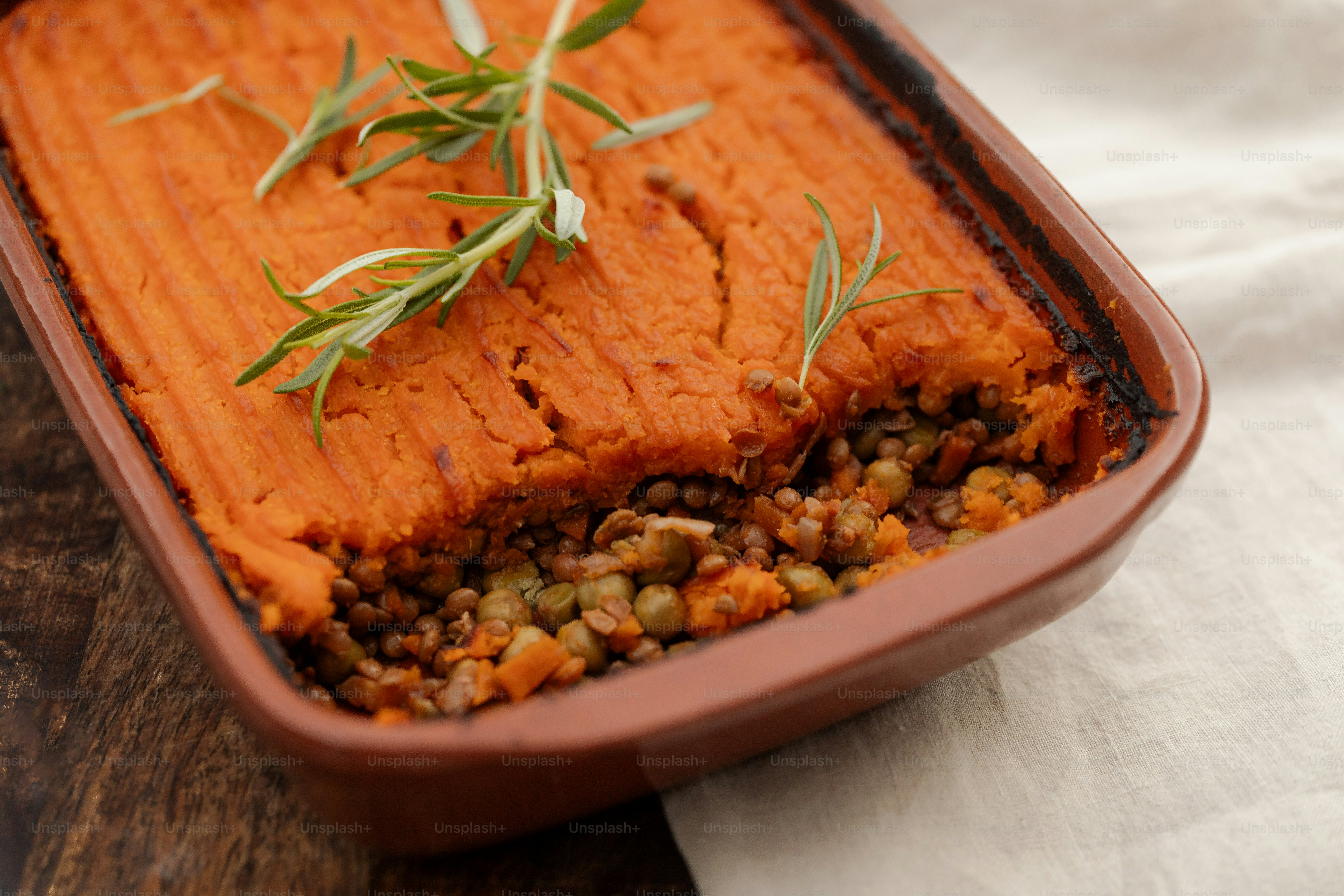 A baked lentil and vegetable casserole topped with mashed sweet potato and rosemary