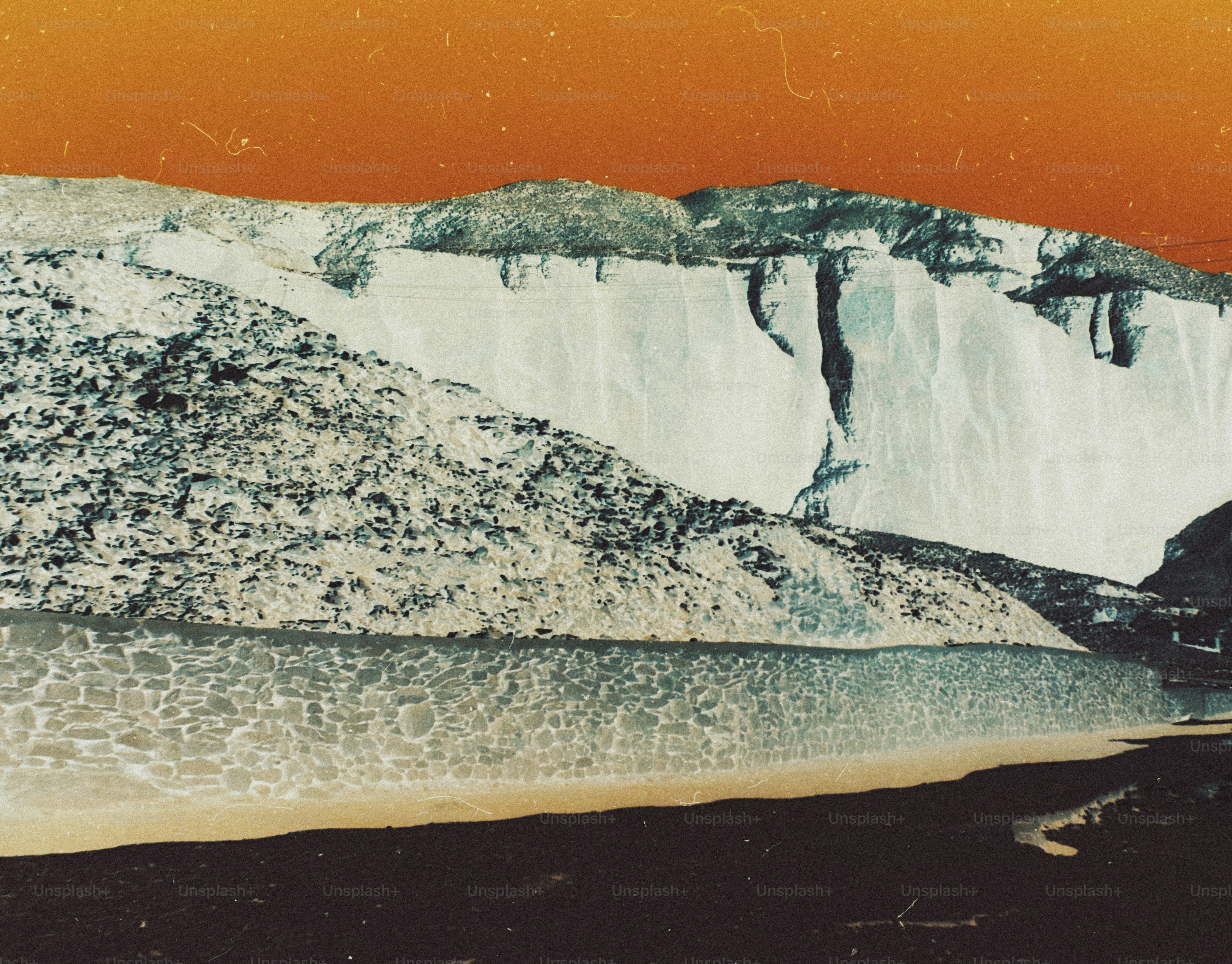 A rocky mountain slope above a stone wall under a vibrant orange sky