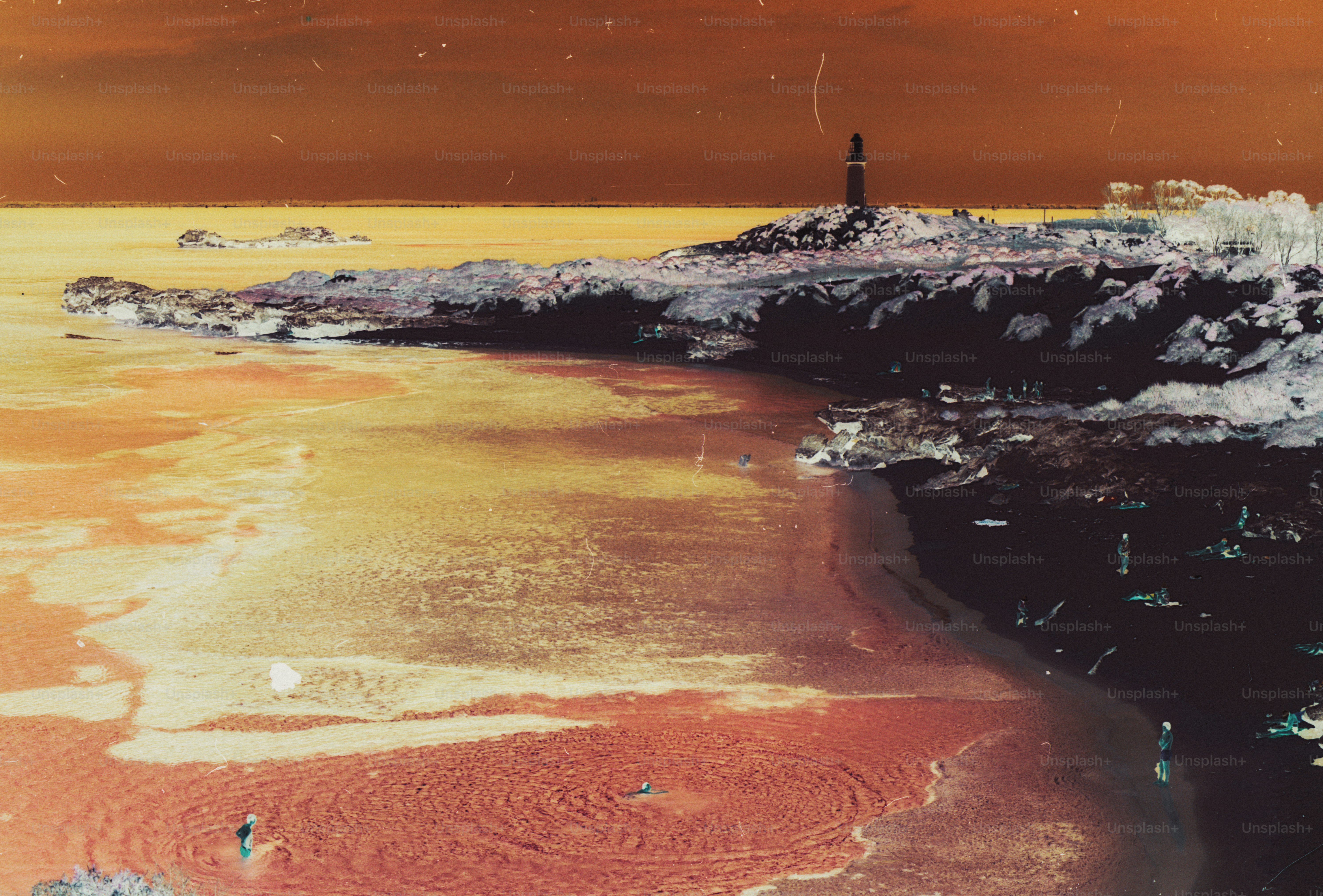 A lighthouse on a rocky coast overlooking a beach with people in the water