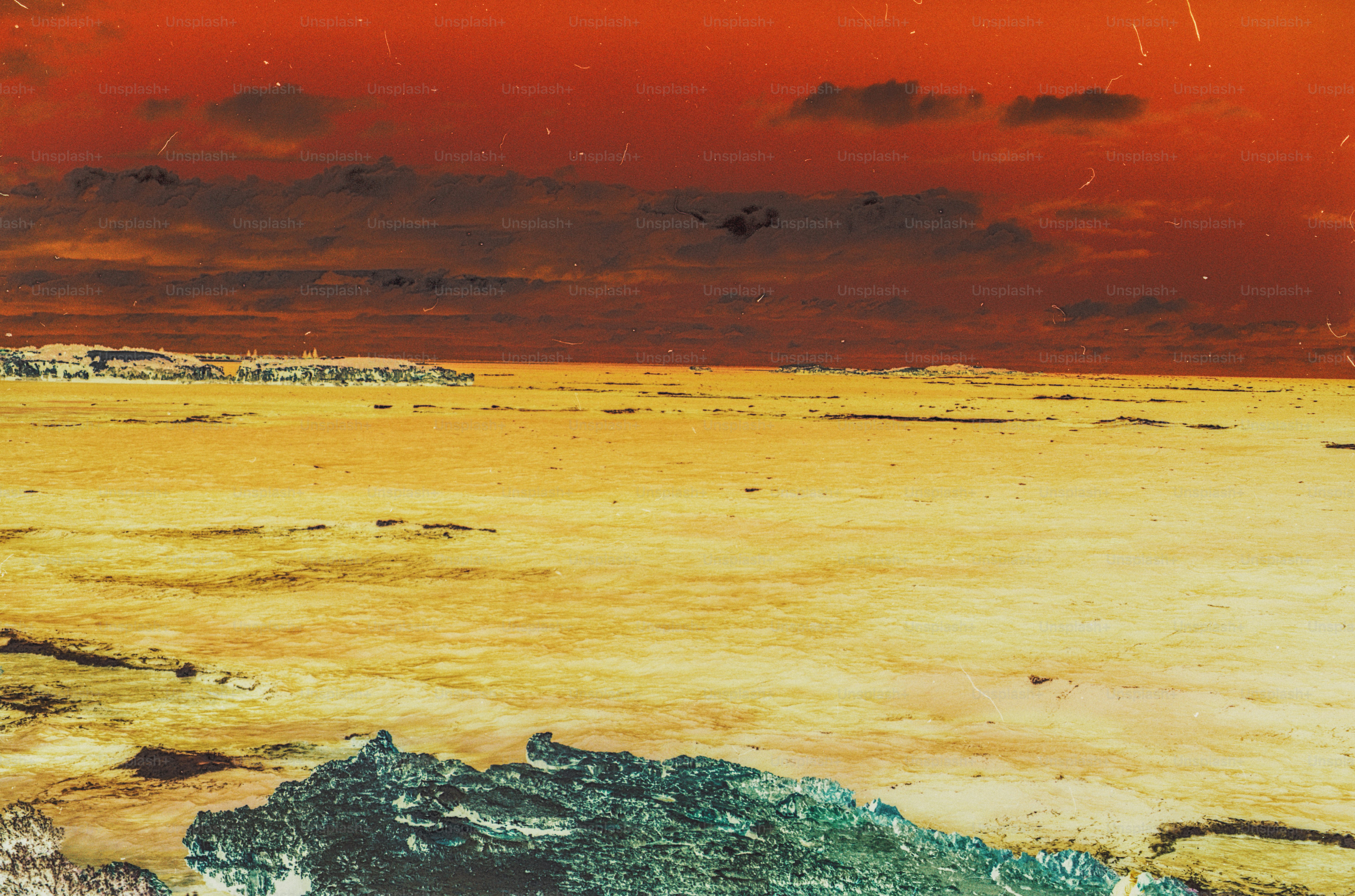 A rocky shoreline meeting a vast yellow sea under a dark red sky