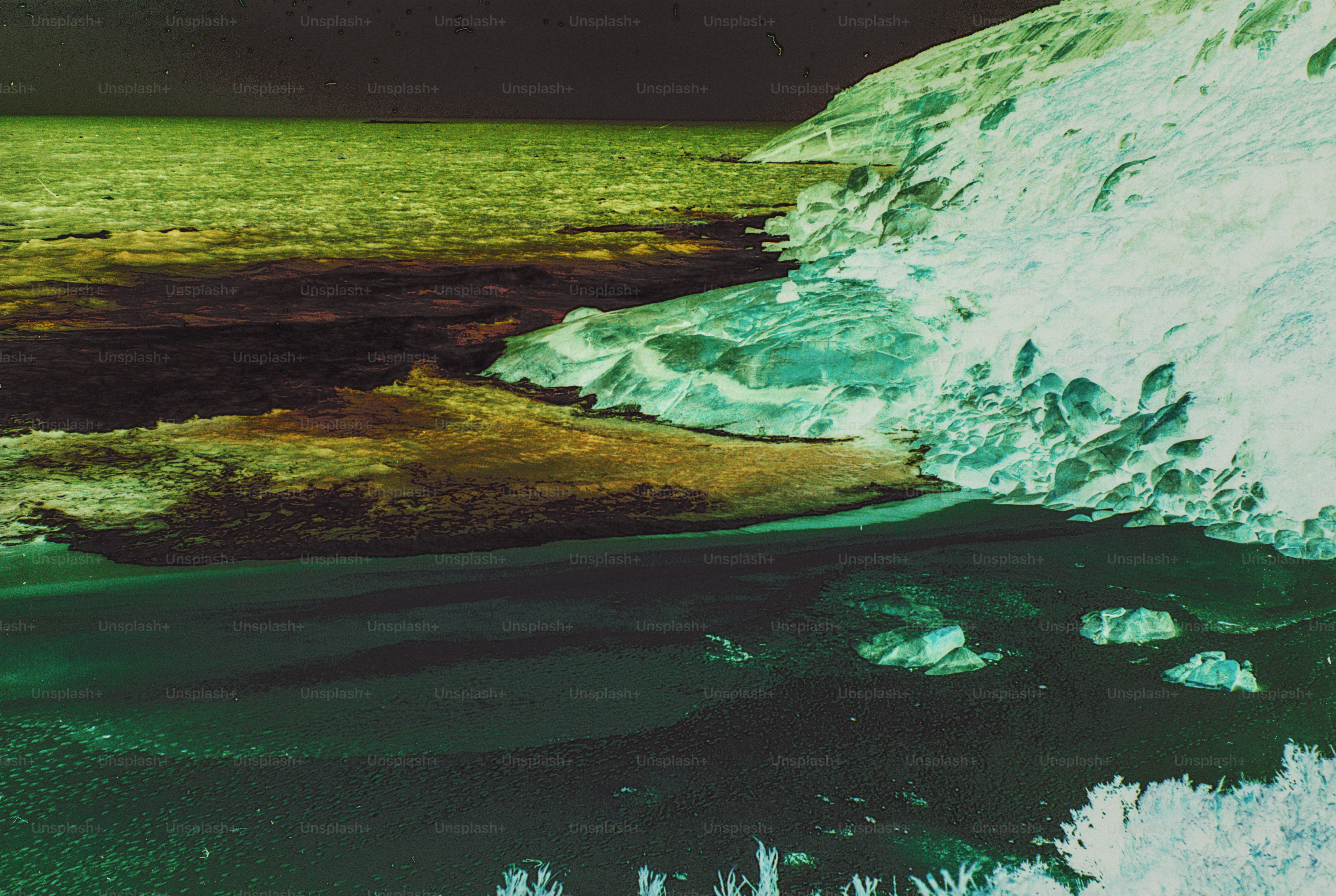 A rocky coastline with dark water and a pale cliff in inverted colors