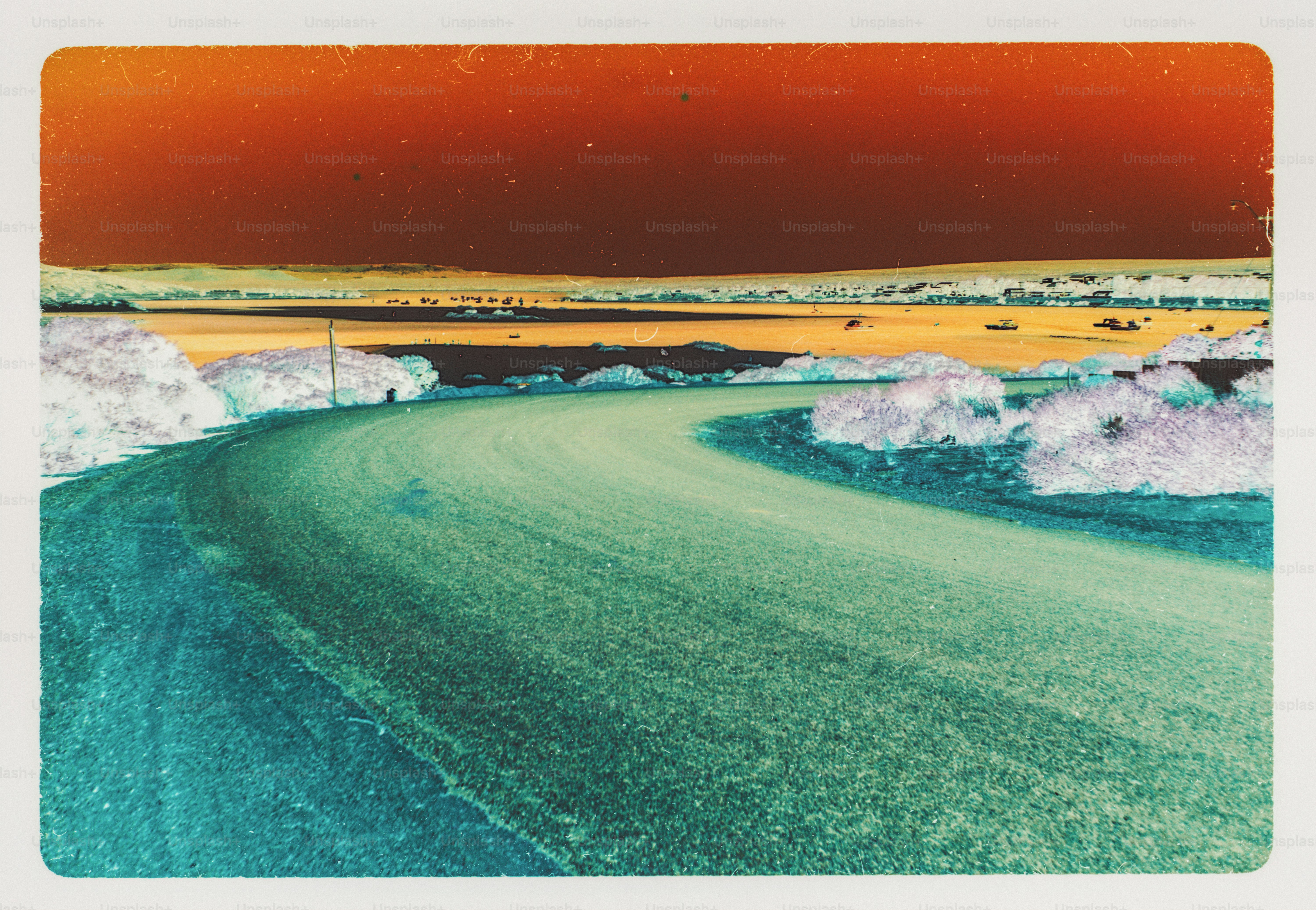 A curved road leading toward a distant coastline under a dark orange sky