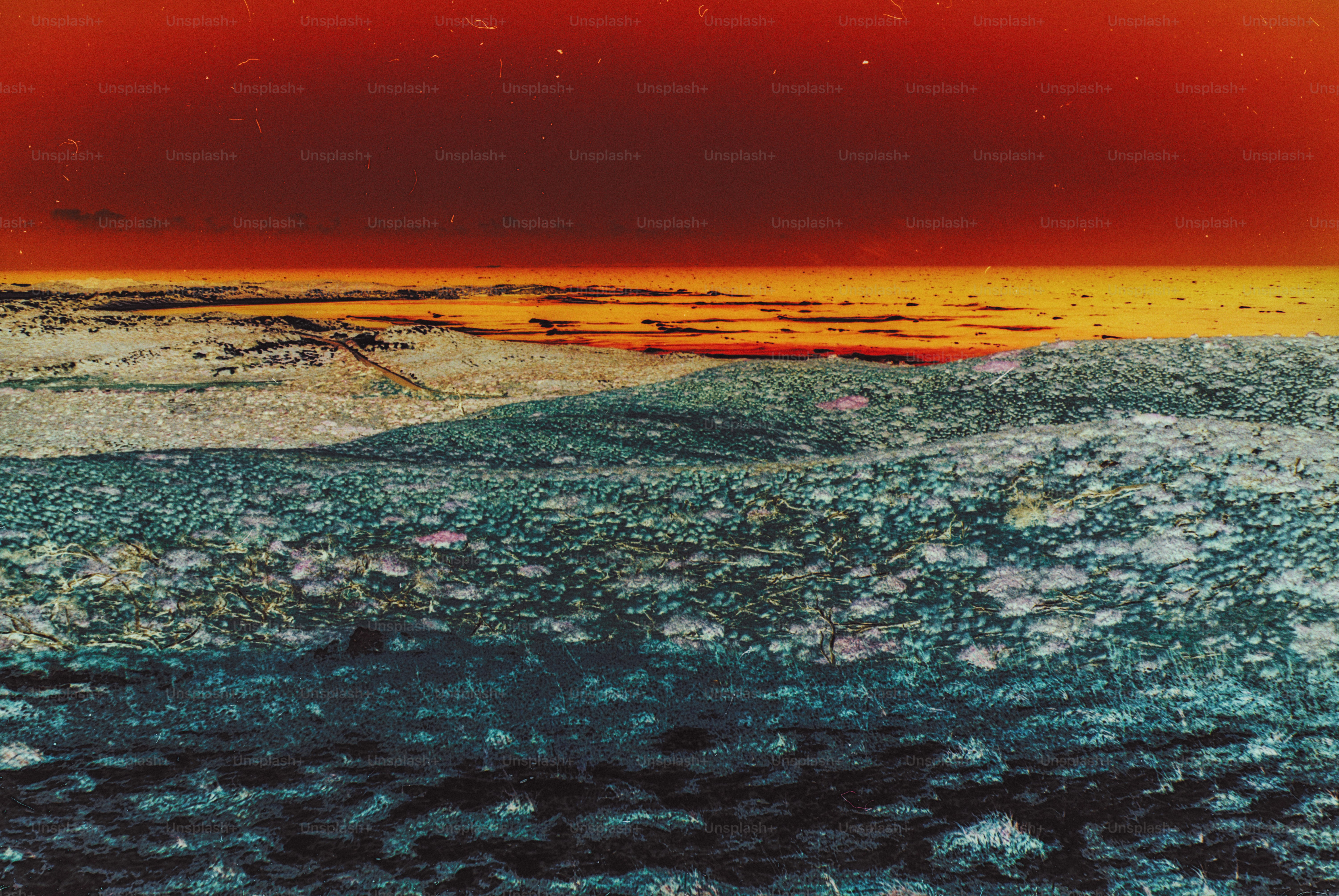 A textured landscape with dark foreground hills under a vibrant red and orange sky