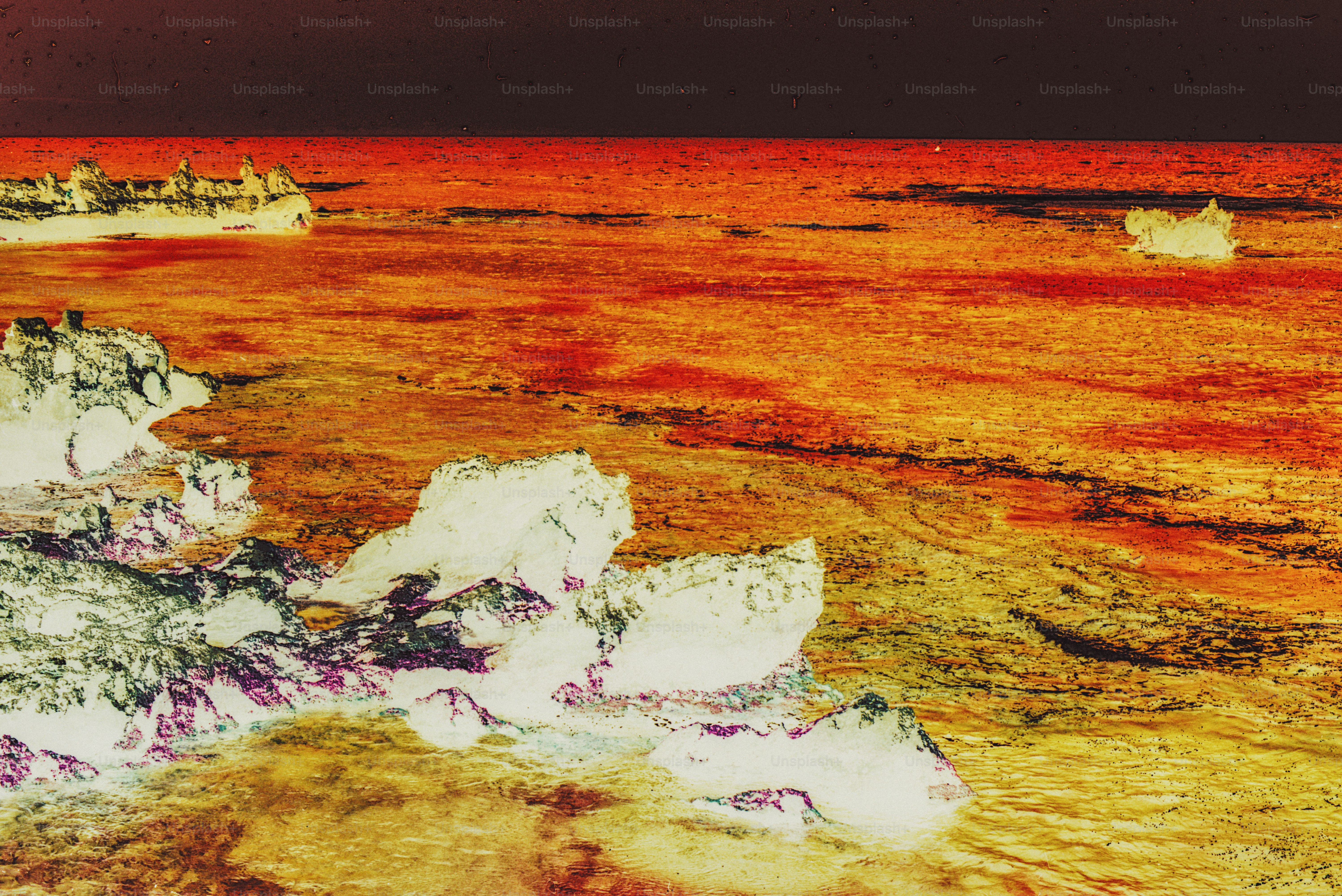 Inverted colors of jagged white rocks along a vibrant orange and red sea