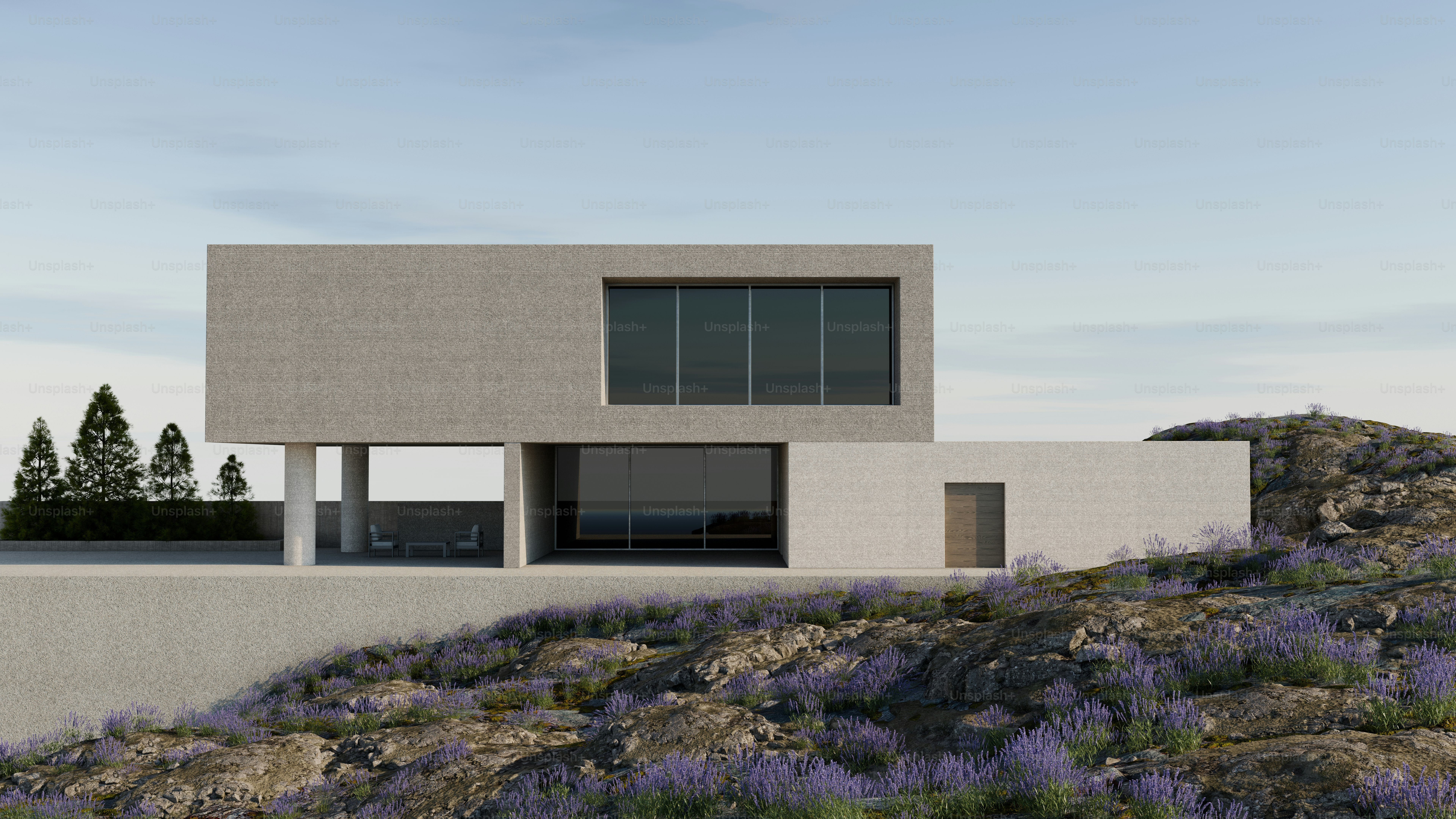 Une maison moderne en béton avec de grandes fenêtres au bord d’une colline rocheuse ornée de fleurs violettes