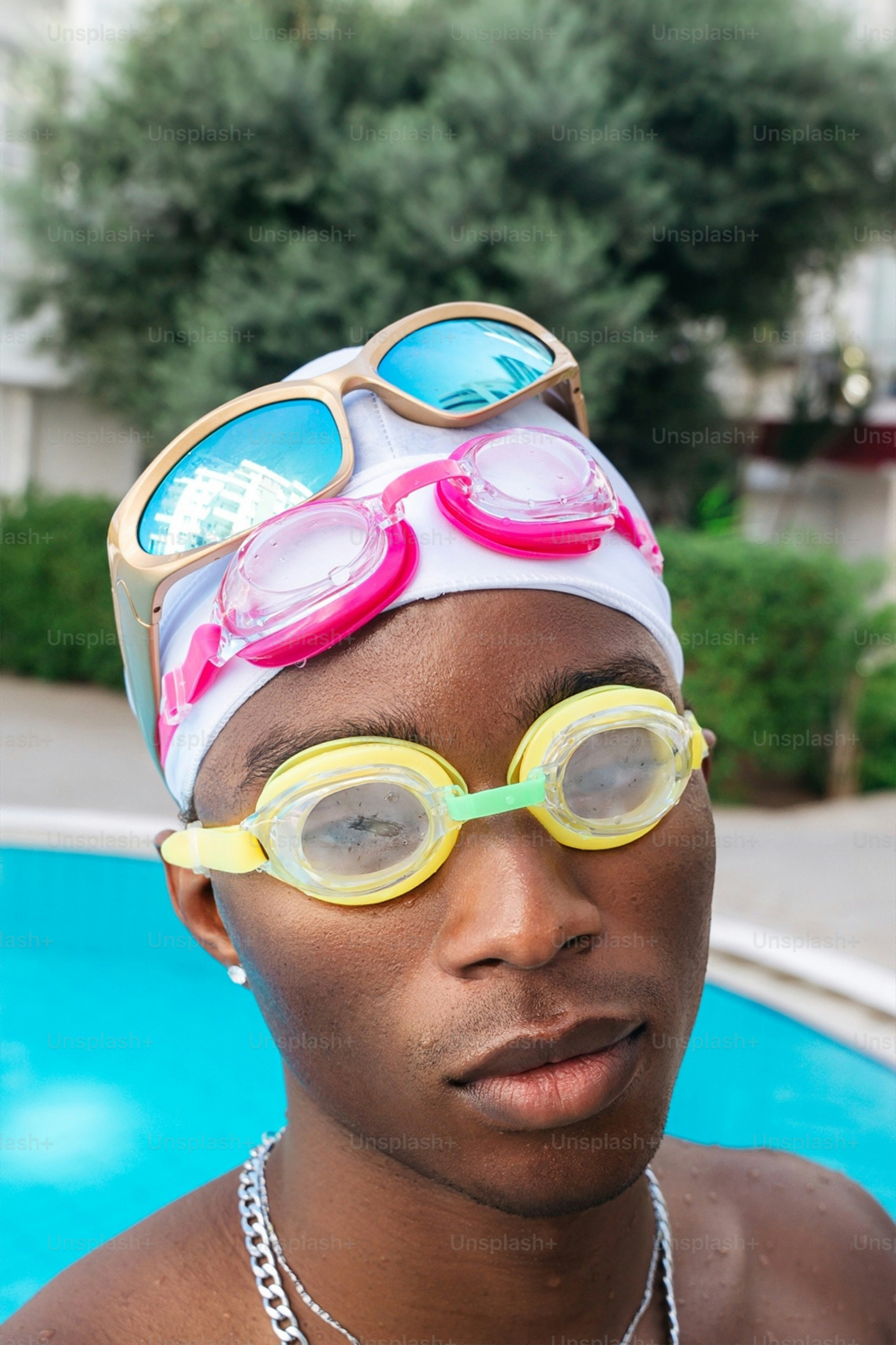 A person wearing a white swim cap, yellow goggles, and pink goggles by a pool