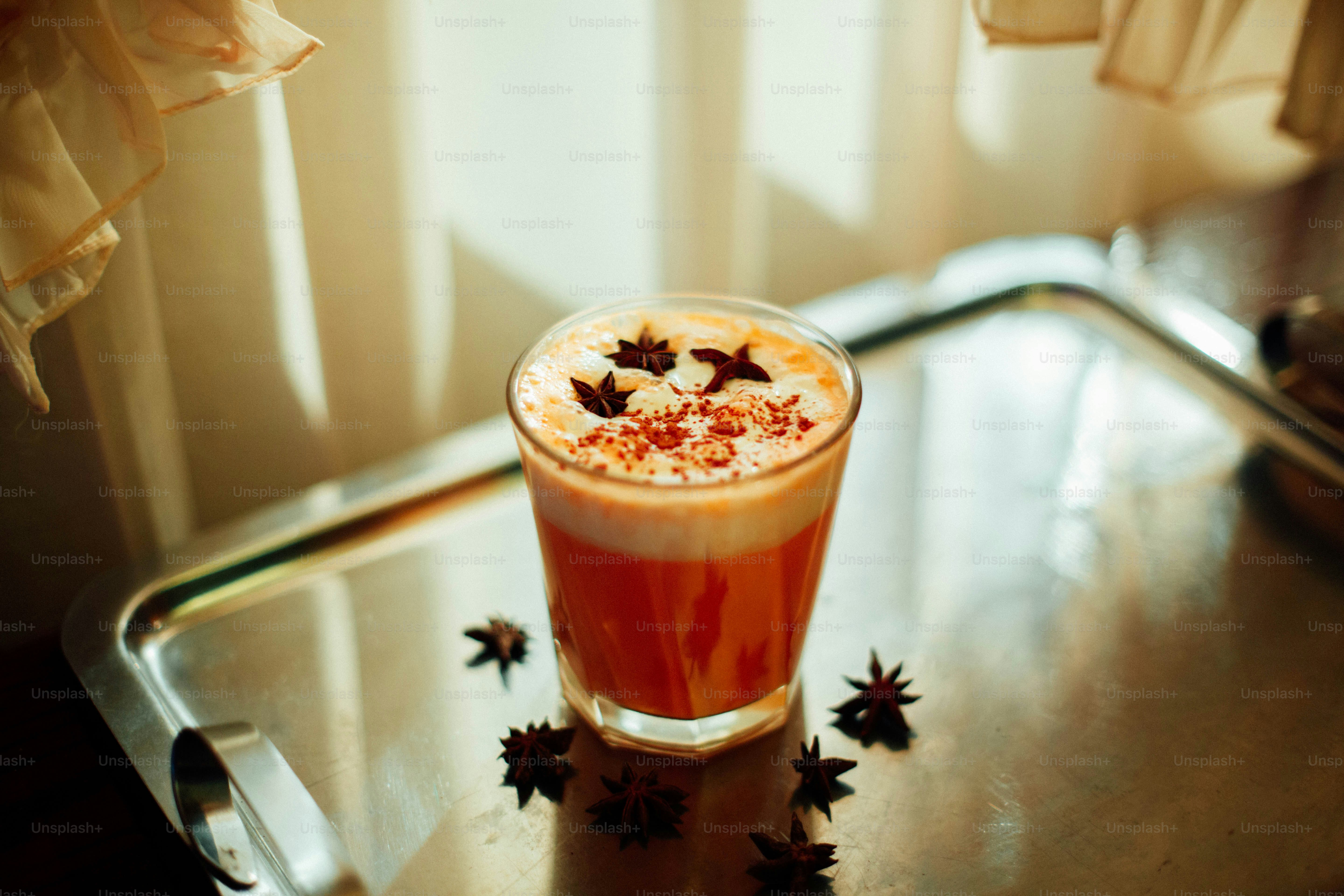 Ein Glas Orange Pumpkin Spice Latte, garniert mit Schaum und Sternanis
